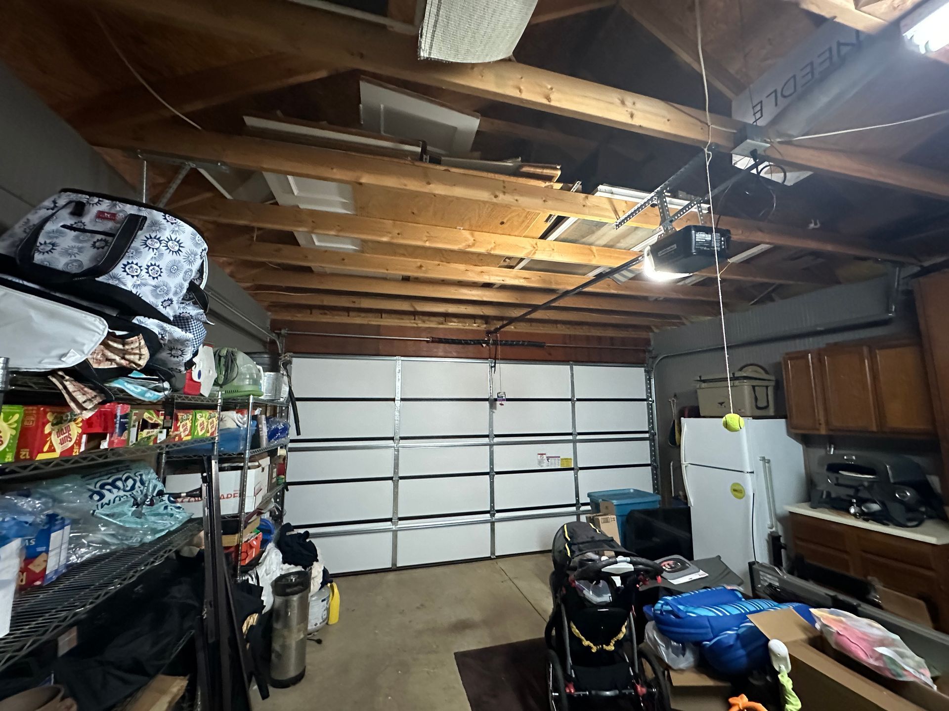 A garage filled with lots of junk and a broken garage door.