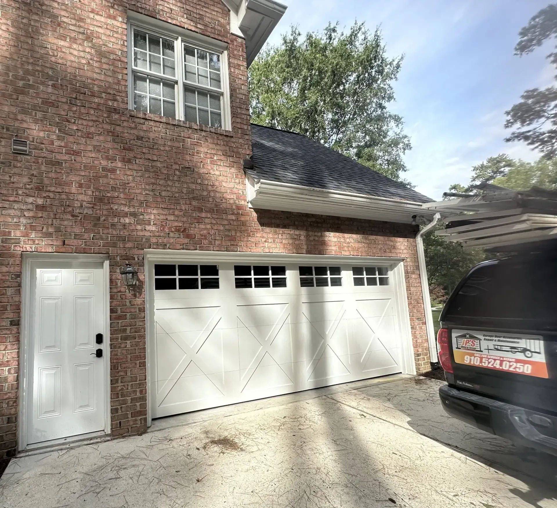 A car is parked in front of a brick house with a white garage door