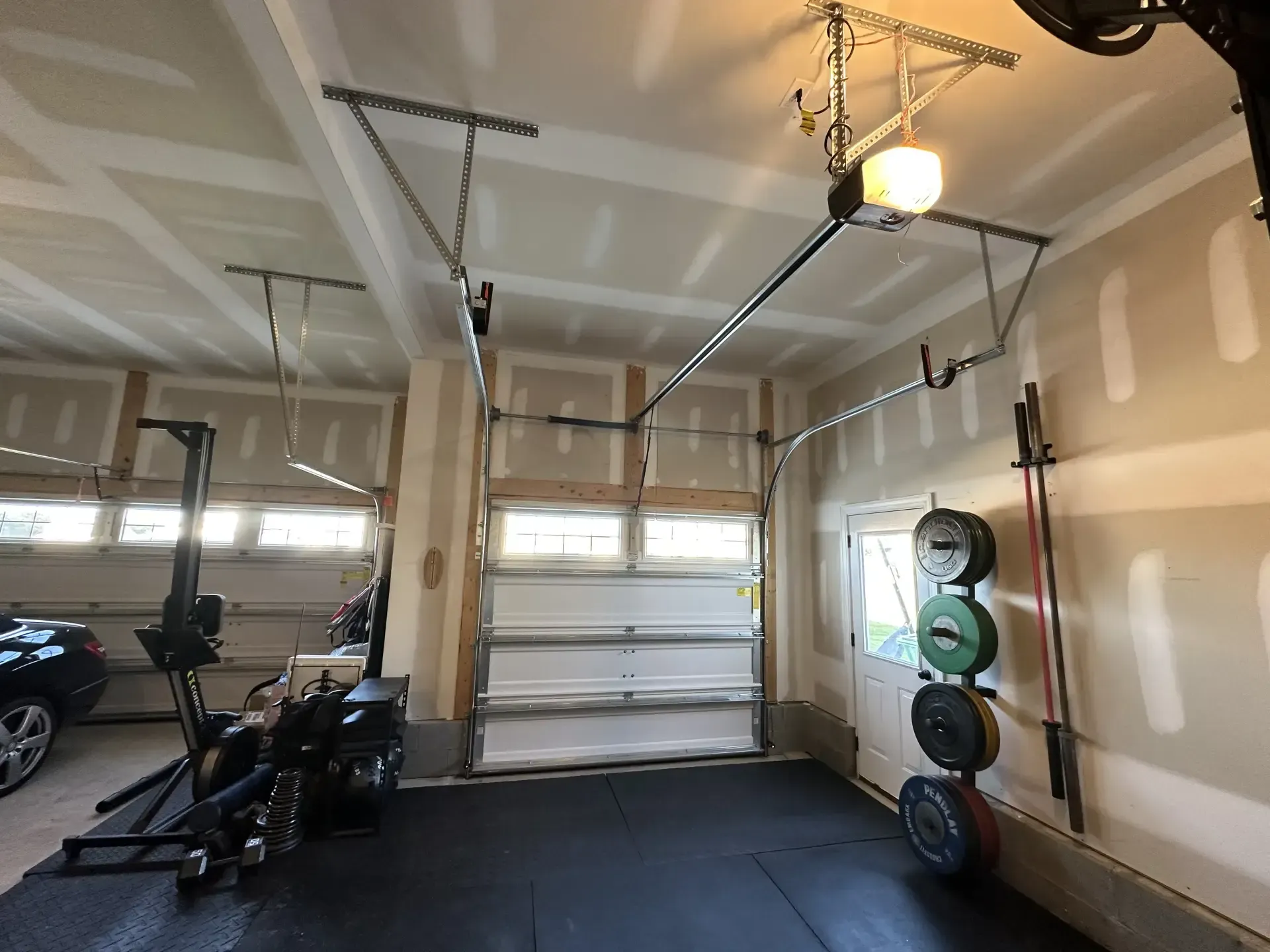 A garage with a garage door open and a row of barbells on the wall