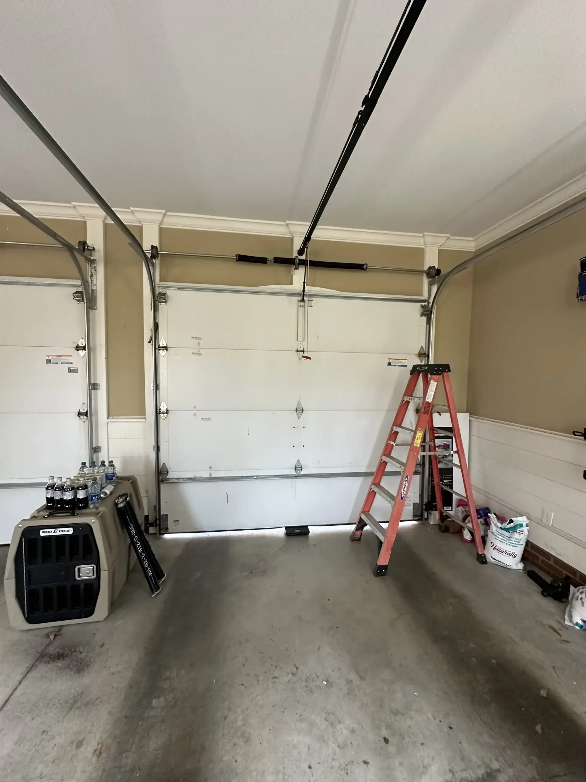 An empty garage with a dog crate and a ladder