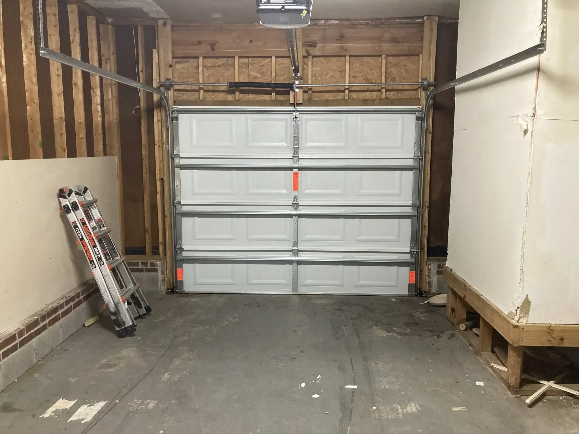 A garage with a garage door open and a ladder on the floor.