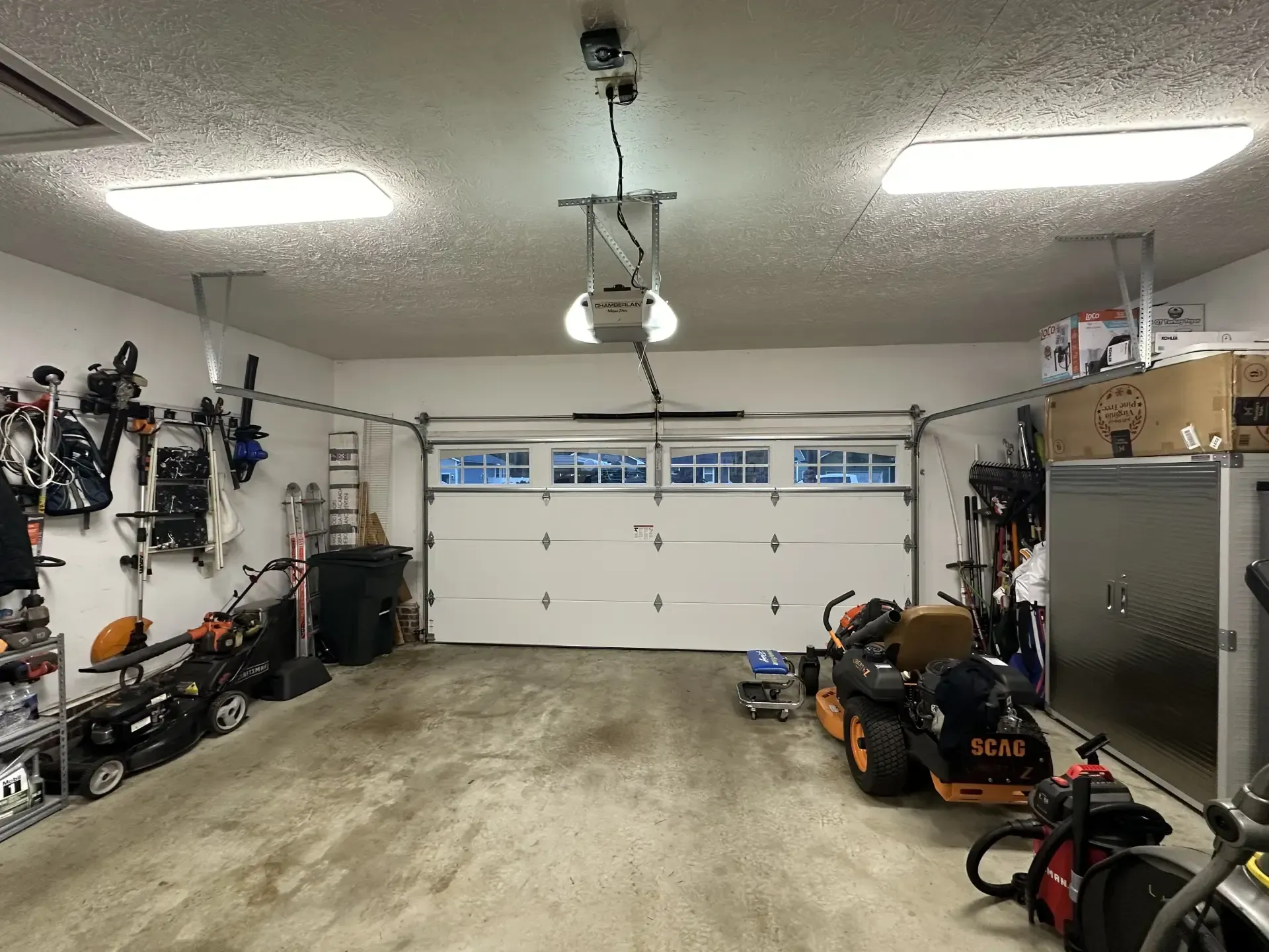 A garage with a garage door open and a lawn mower in it