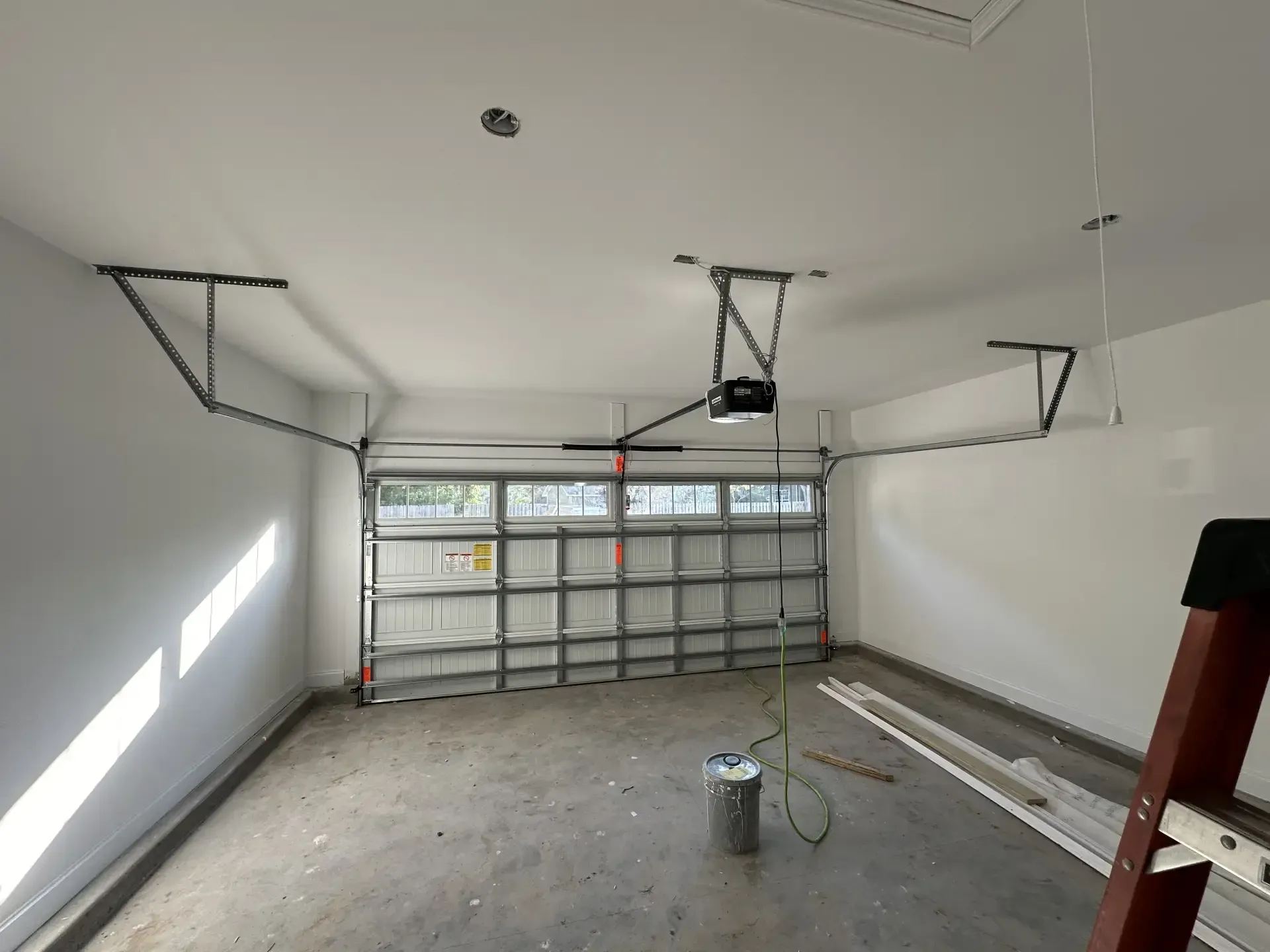 An empty garage with a garage door open and a ladder.
