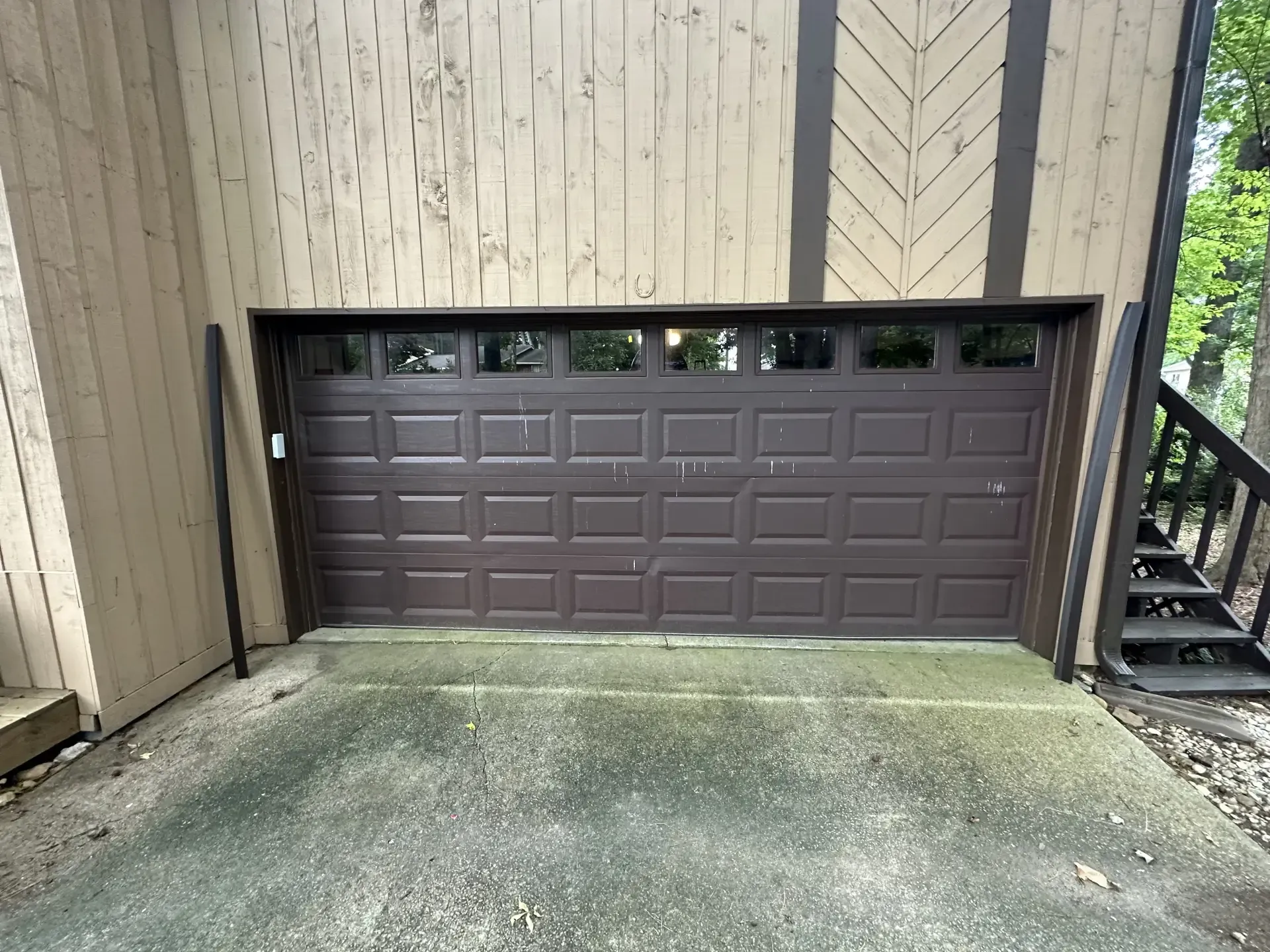 A brown garage door is sitting under a wooden house.