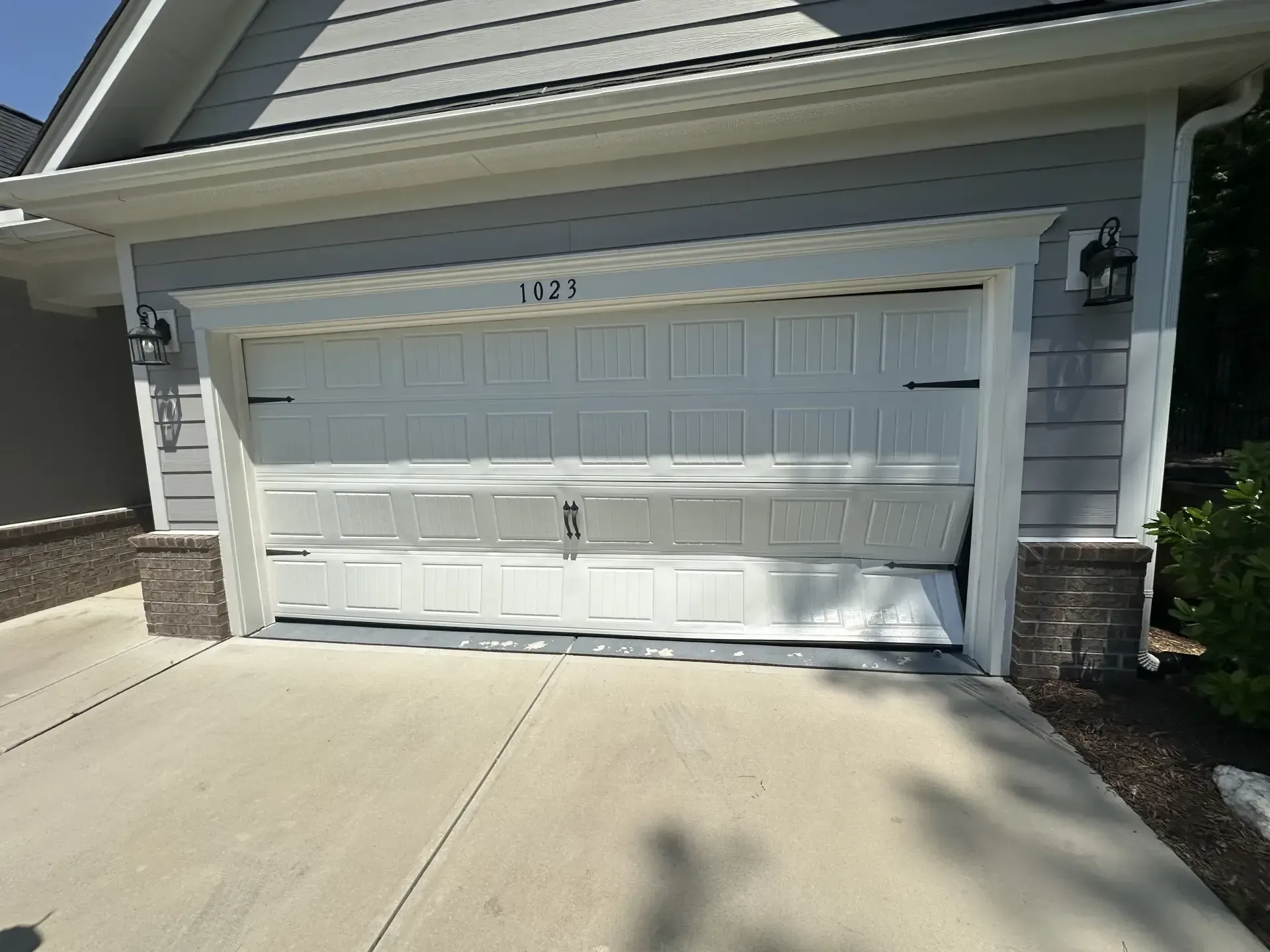 A white garage door is open and locked in front of a house.