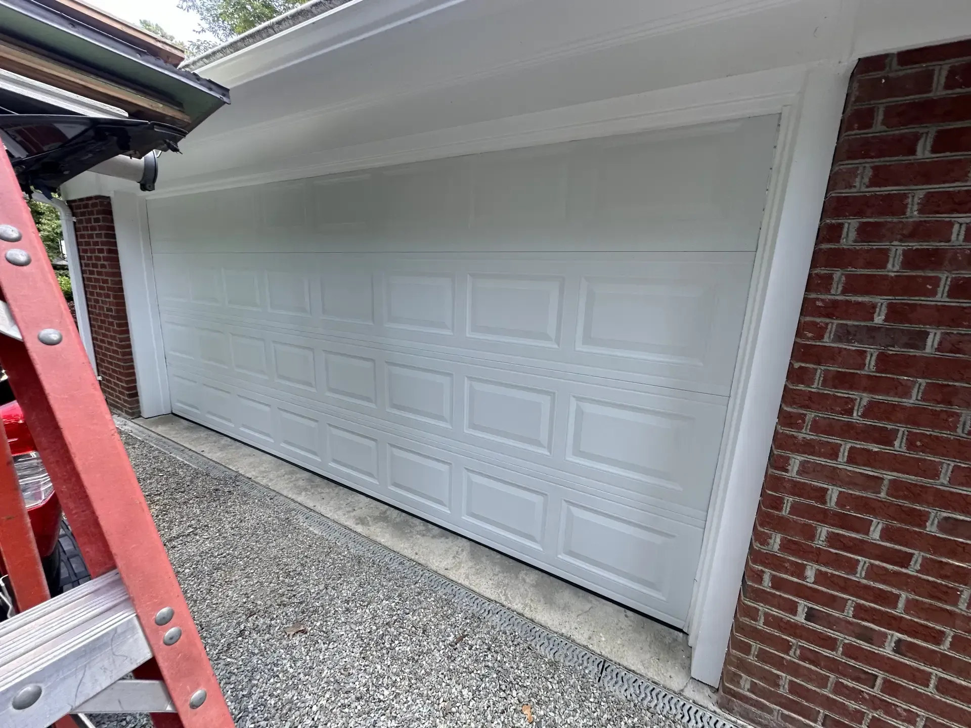 A white garage door is sitting next to a red ladder.