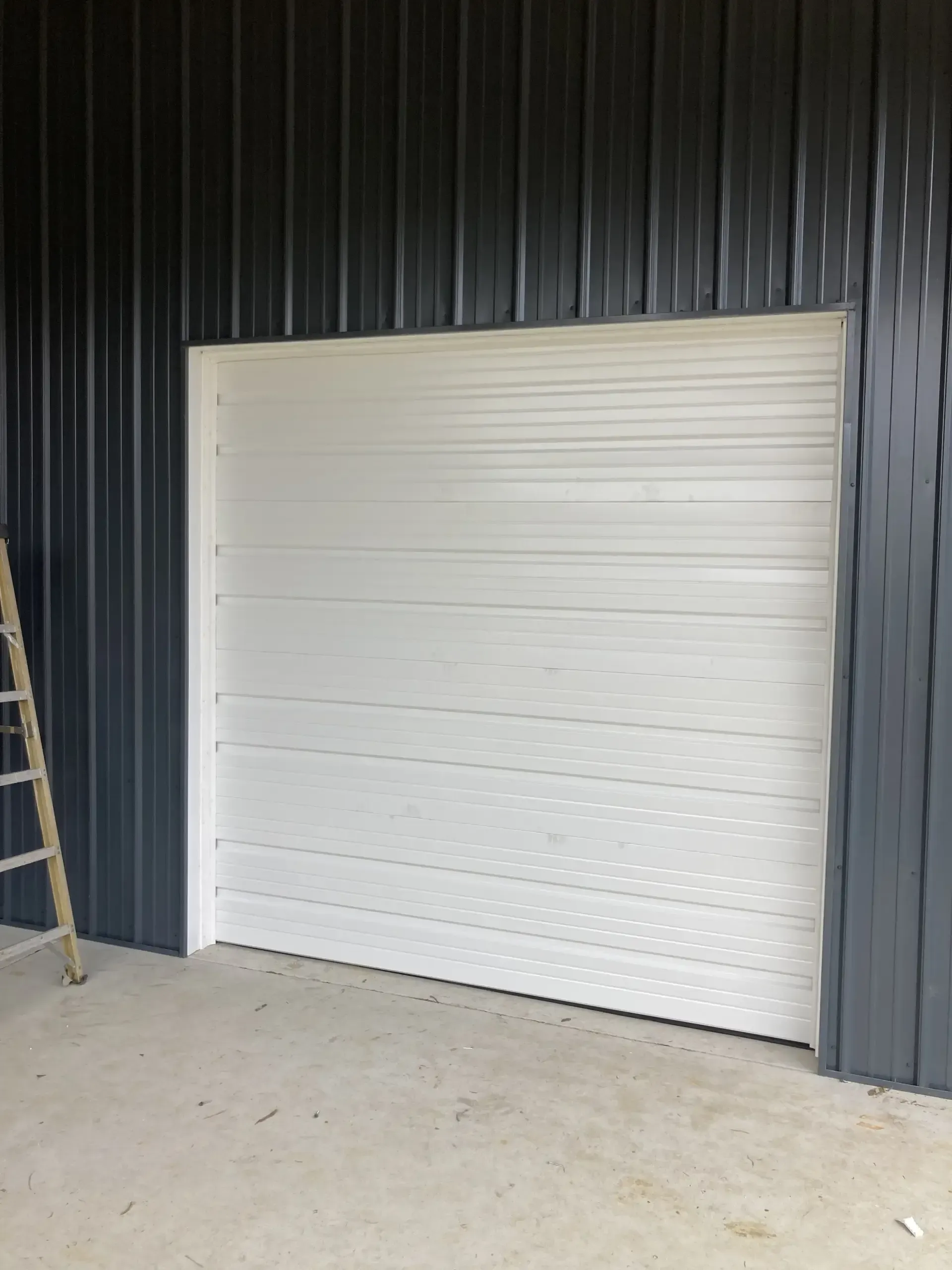 A white garage door is sitting on the side of a building next to a ladder.