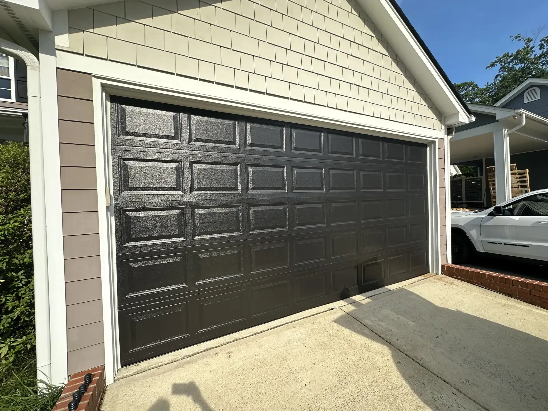 A black garage door is open and a white car is parked in front of it.