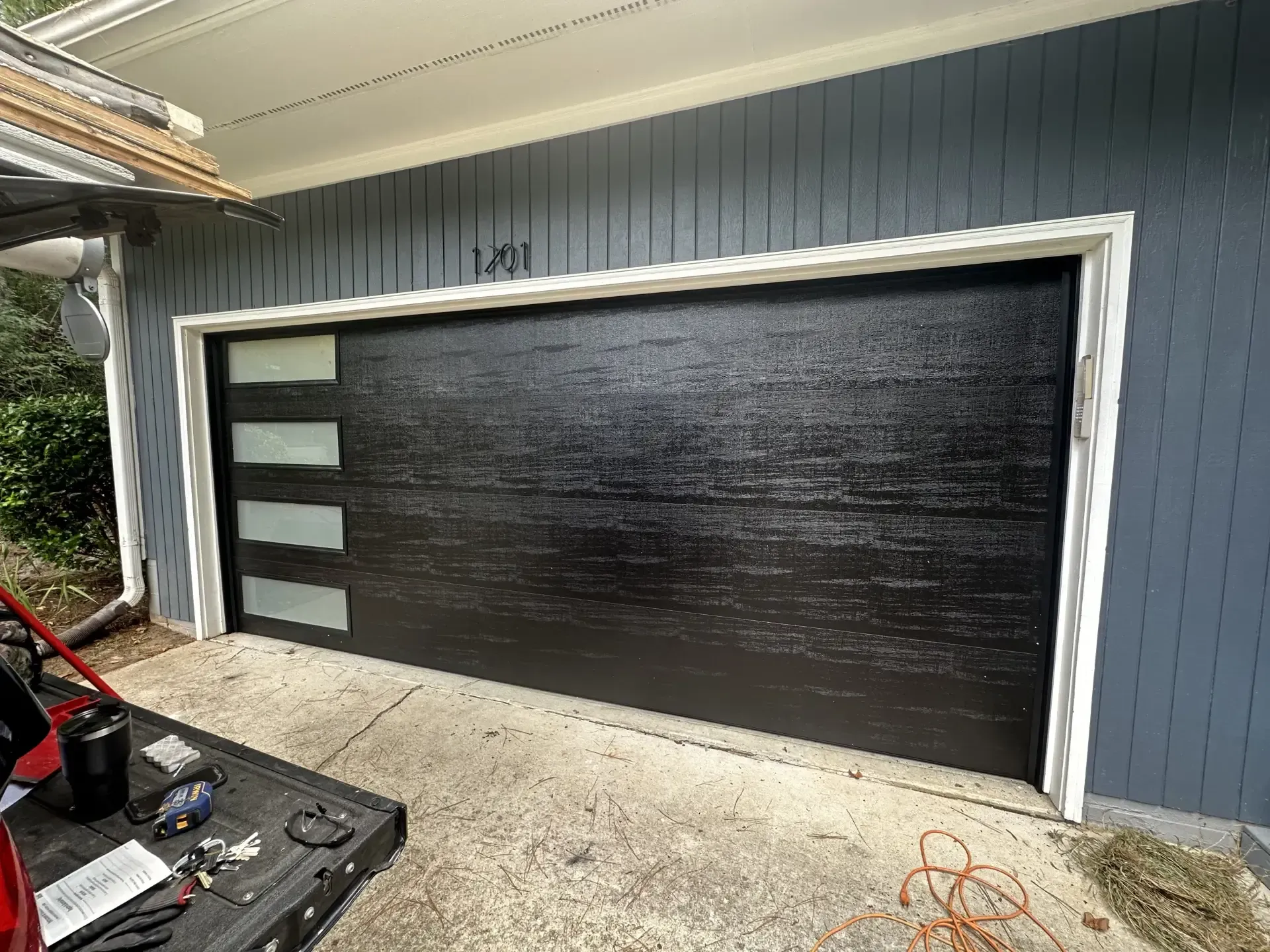 A black garage door is being installed on a blue house.