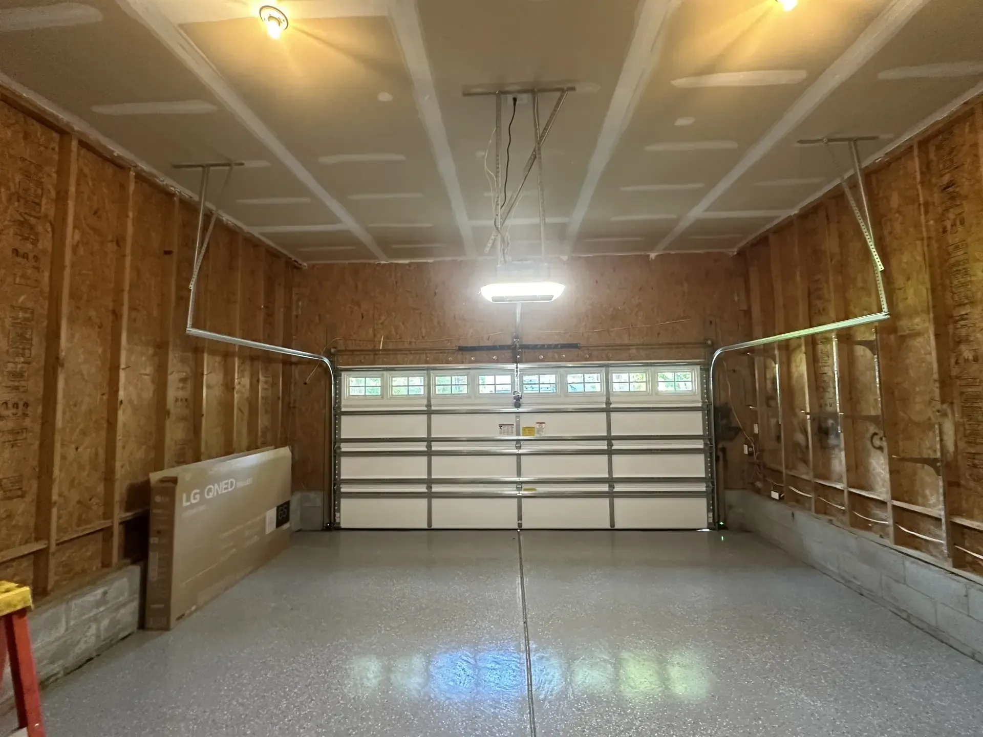An empty garage with a garage door open and a light on the ceiling.