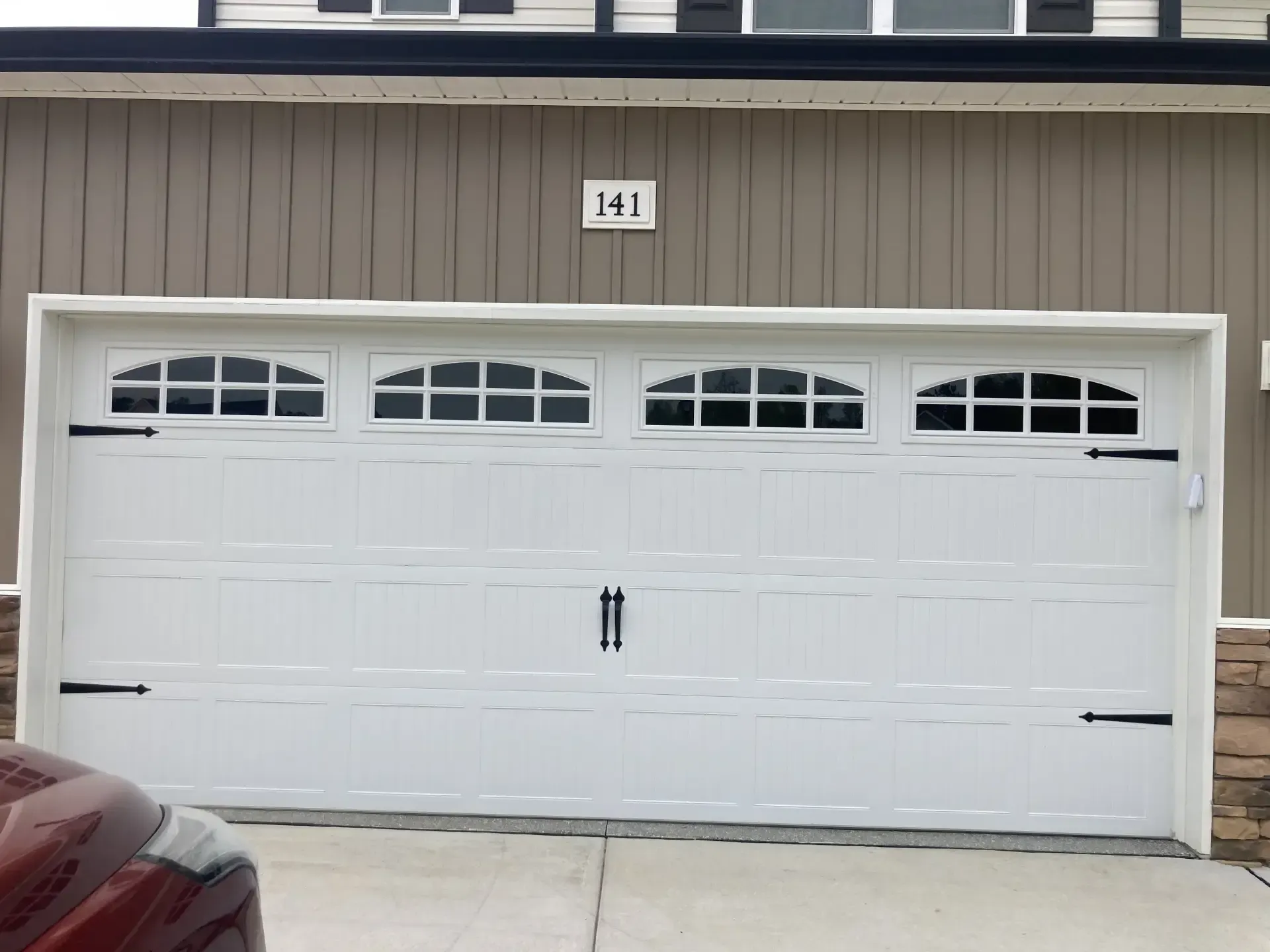 A white garage door is sitting in front of a brown house.