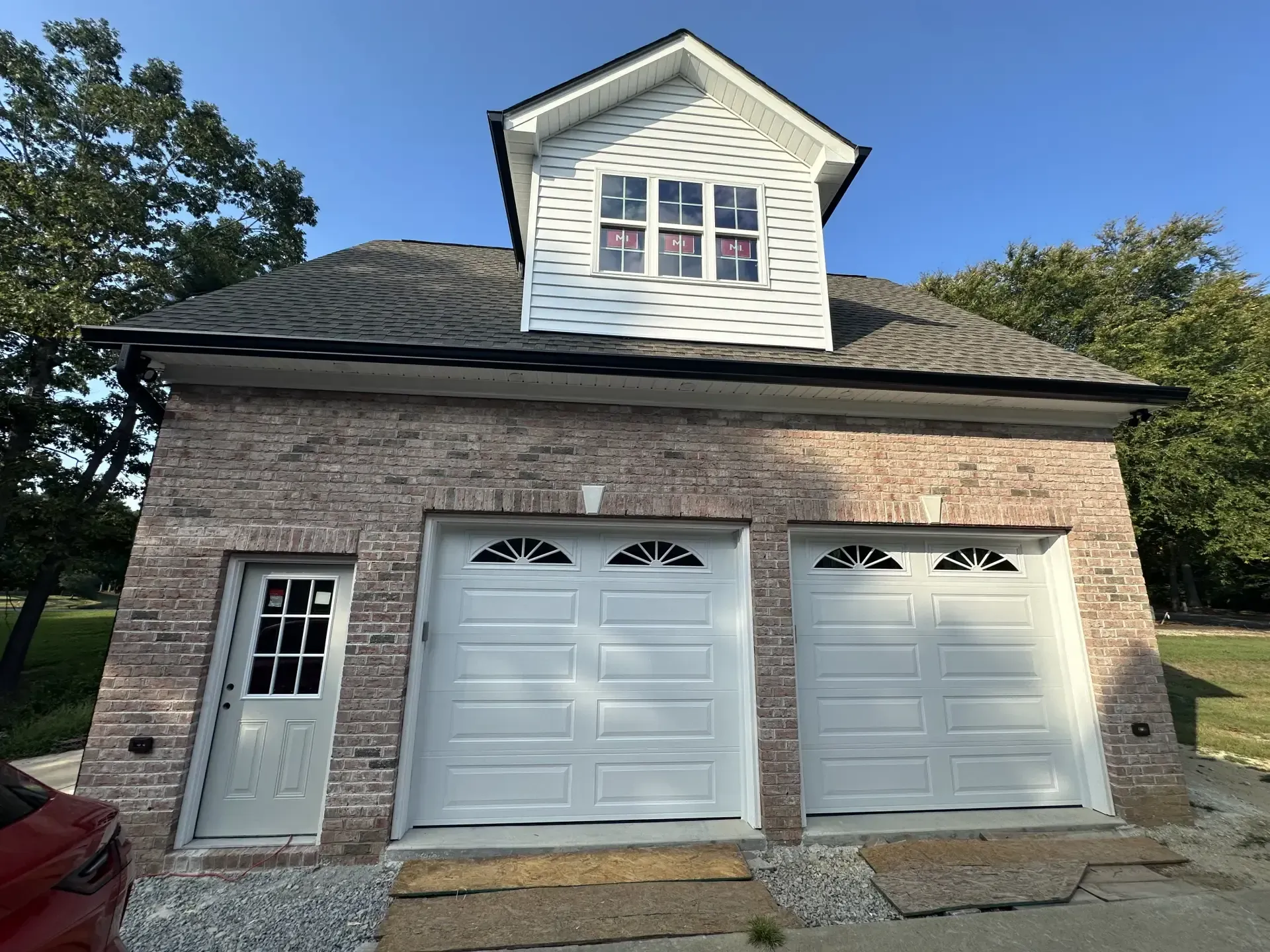 A brick garage with three white garage doors and a white roof