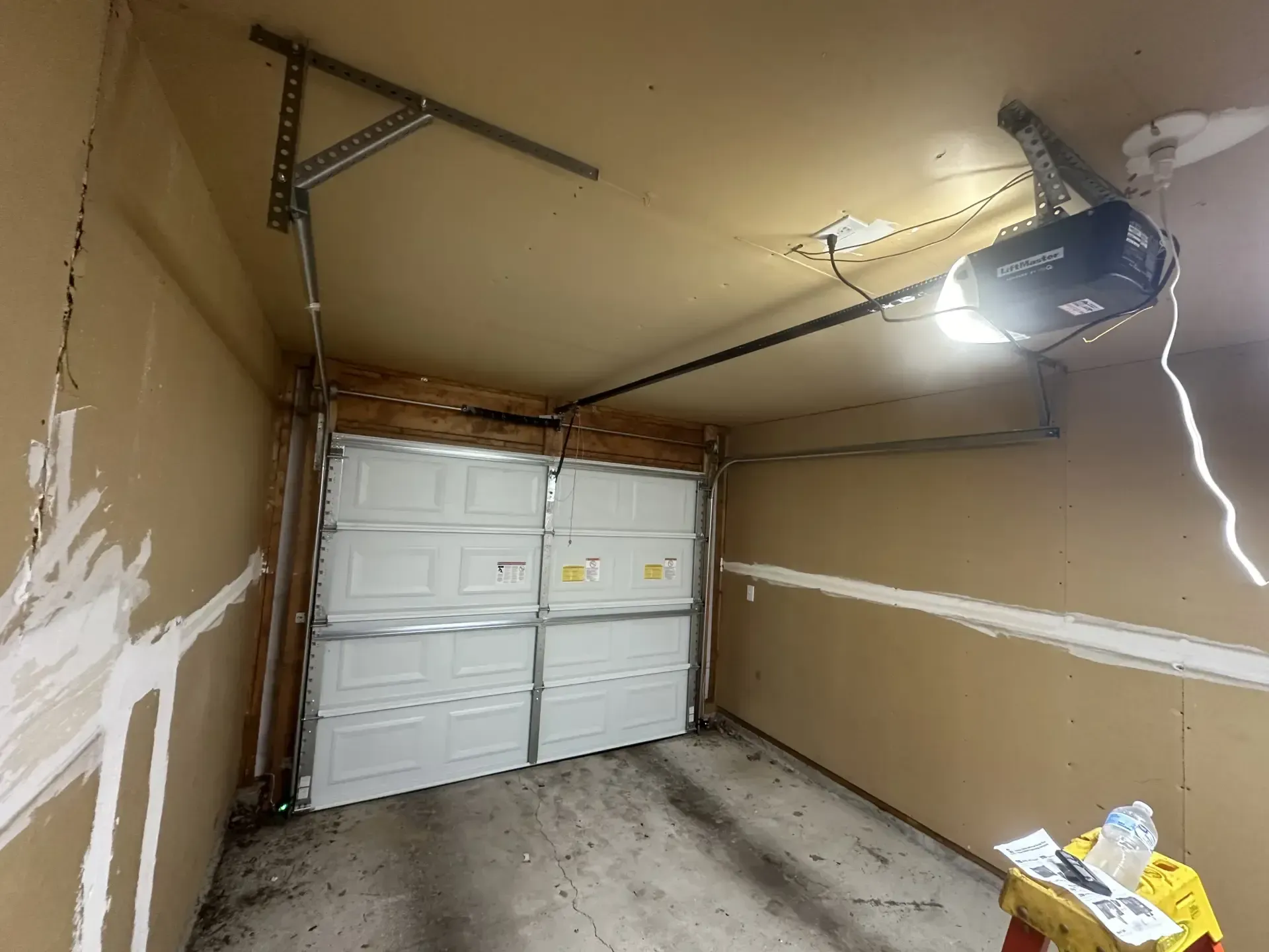 A garage with a garage door open and a garage door opener hanging from the ceiling.