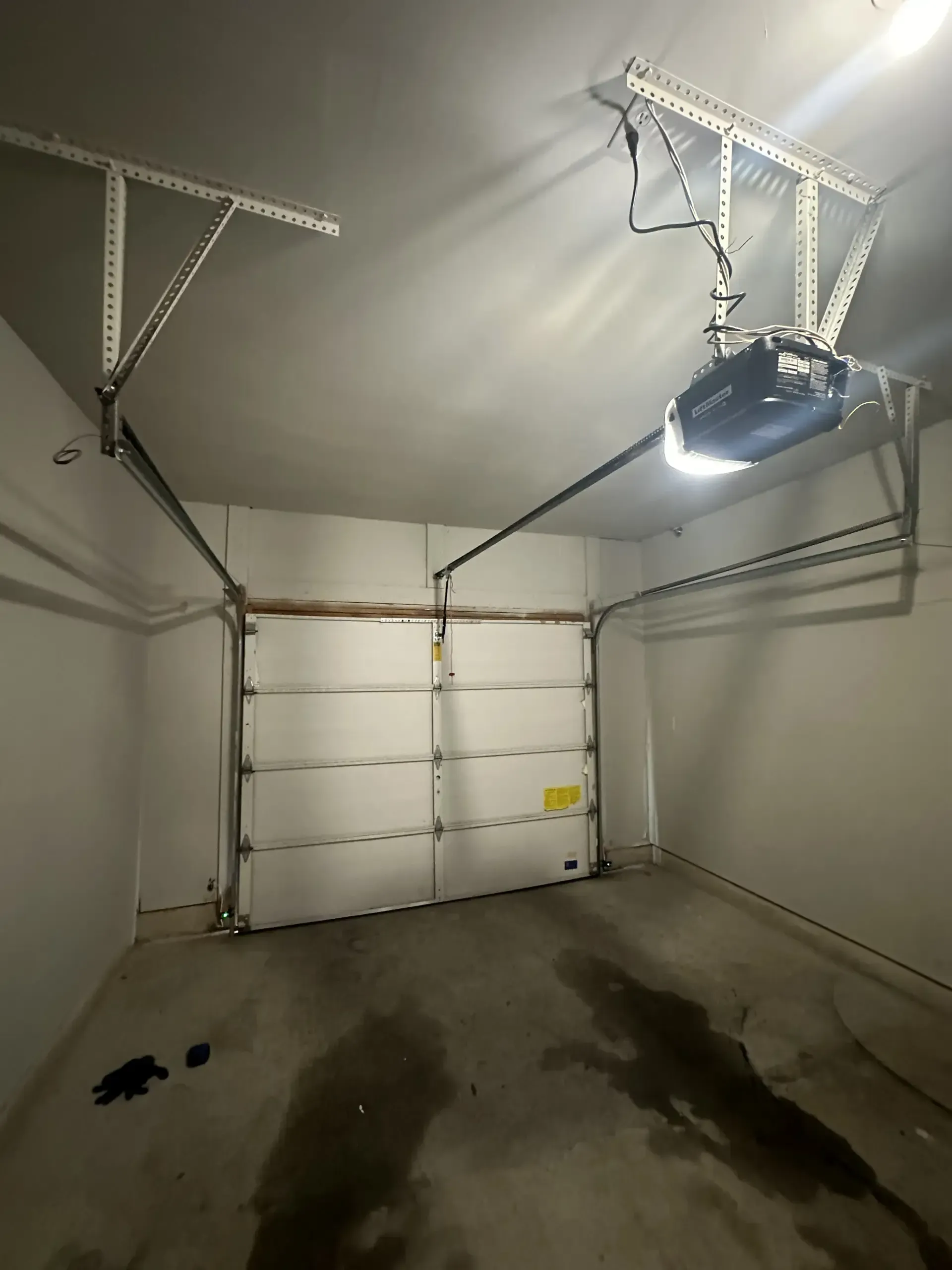 An empty garage with a garage door open and a garage door opener hanging from the ceiling.