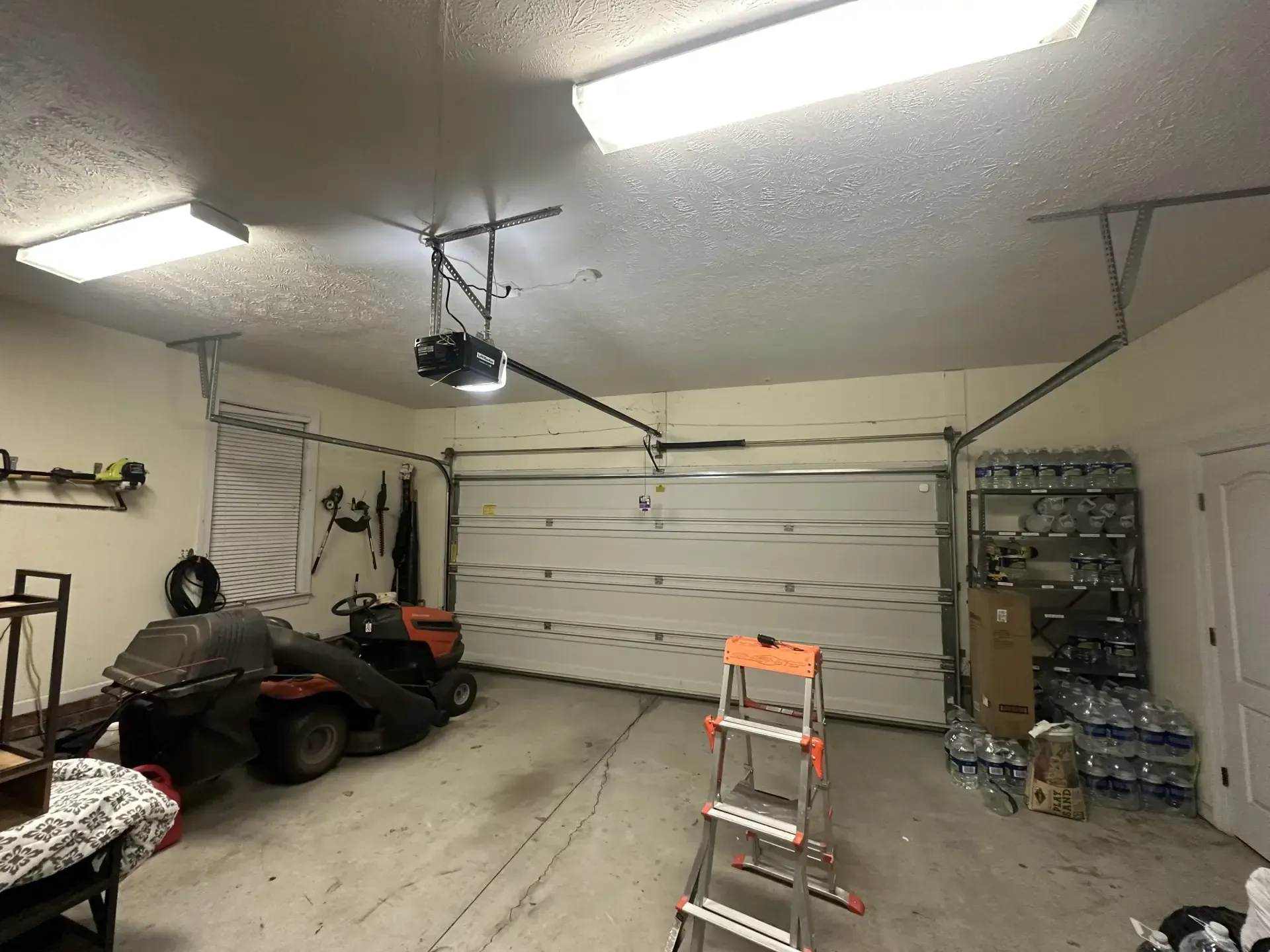 A garage with a lawn mower and a ladder in it.