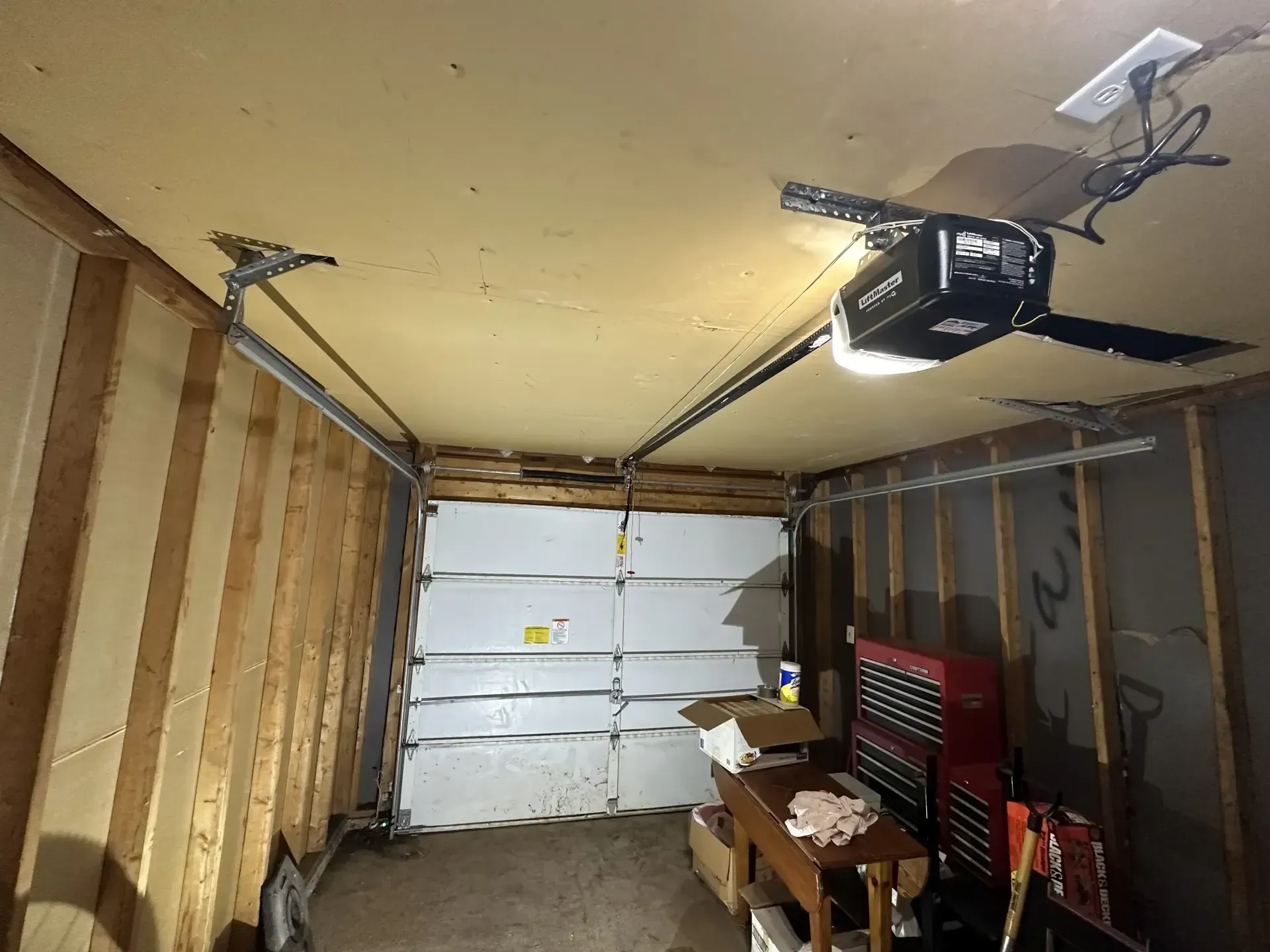A garage with a garage door open and a garage door opener hanging from the ceiling.