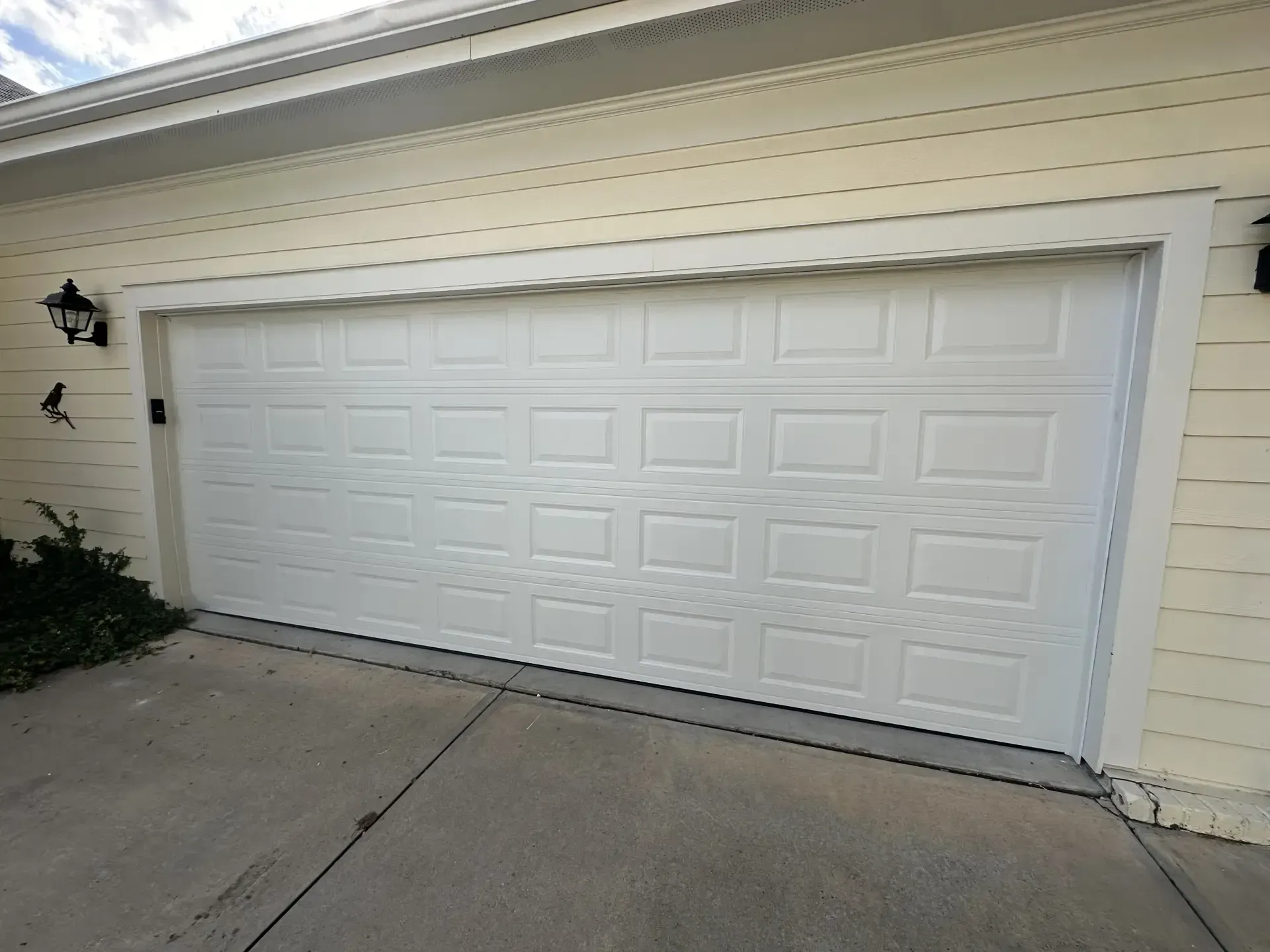 A white garage door is sitting in front of a white house.