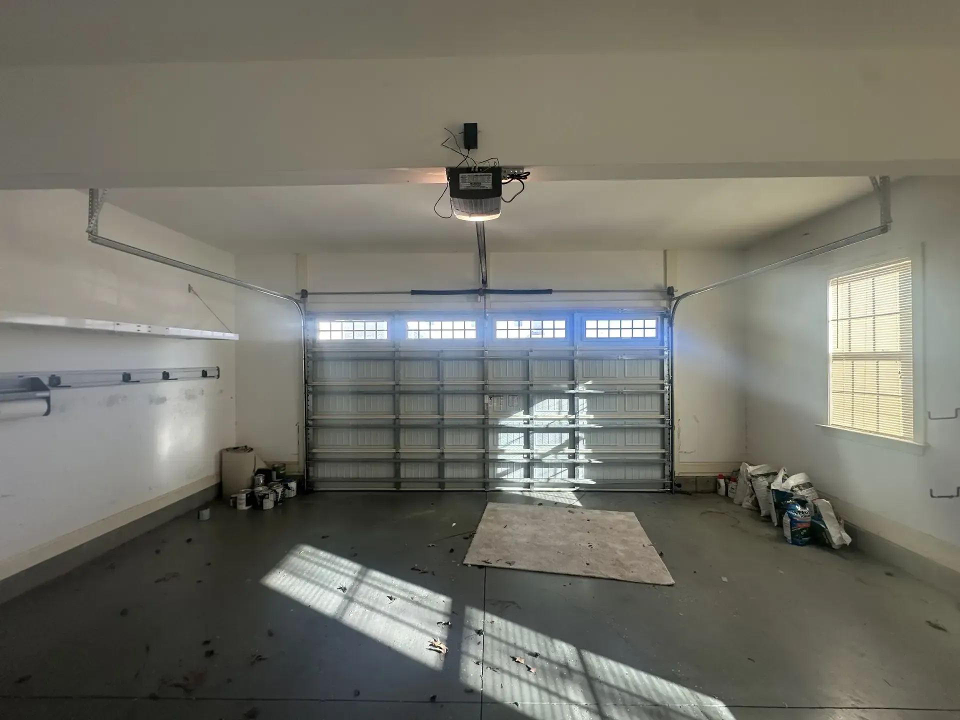 An empty garage with a garage door open and a rug on the floor.