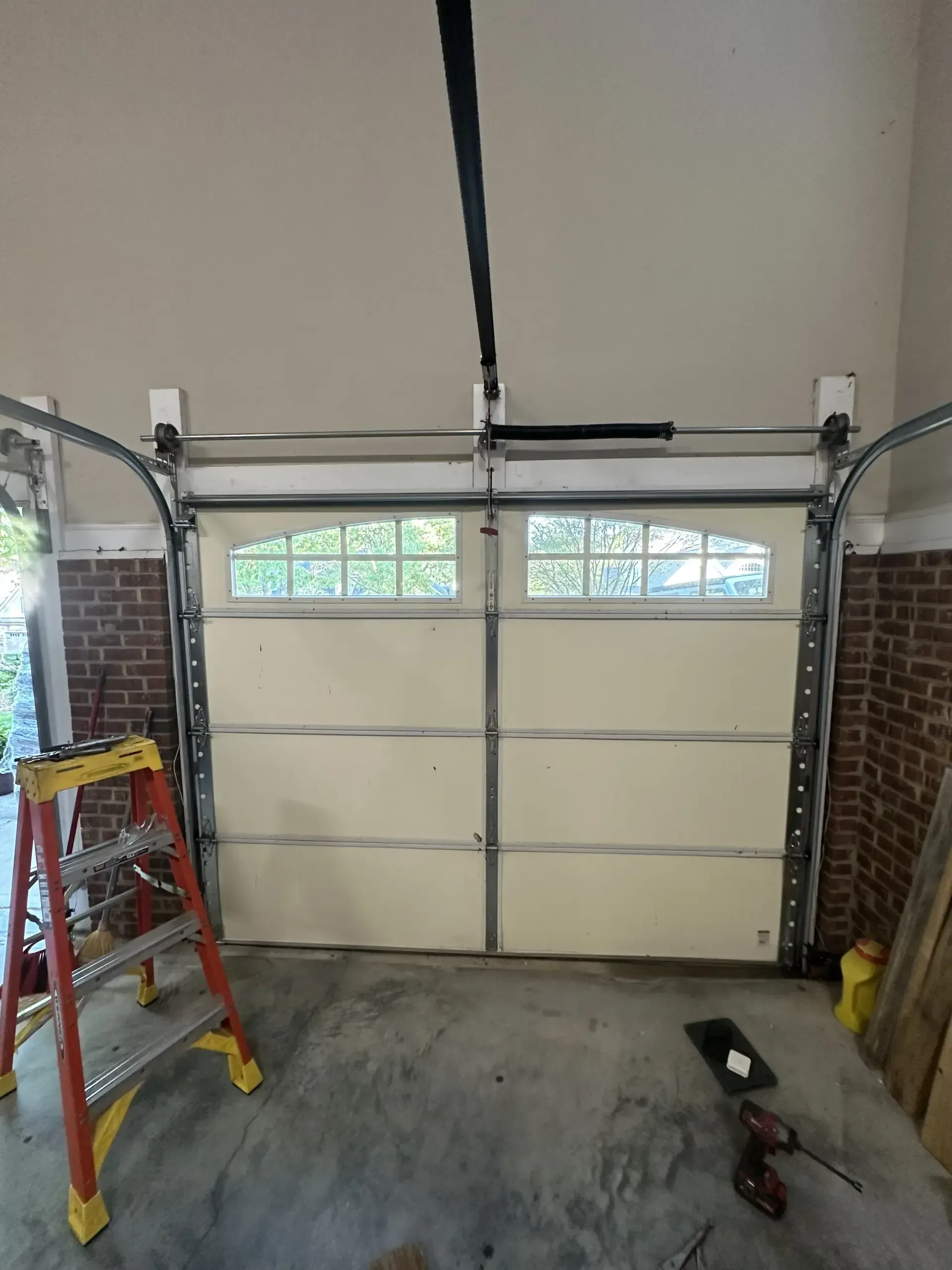 A garage door is being repaired in a garage with a ladder.