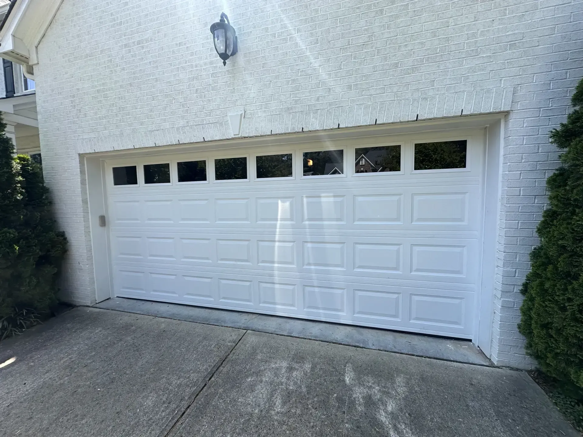 A white garage door is open in front of a white brick house.