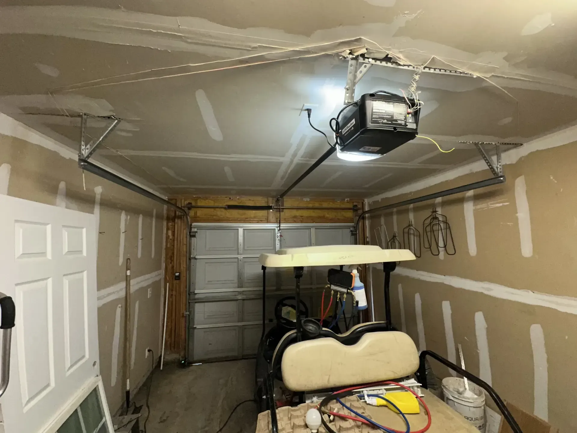 A golf cart is parked in a garage with a garage door open.