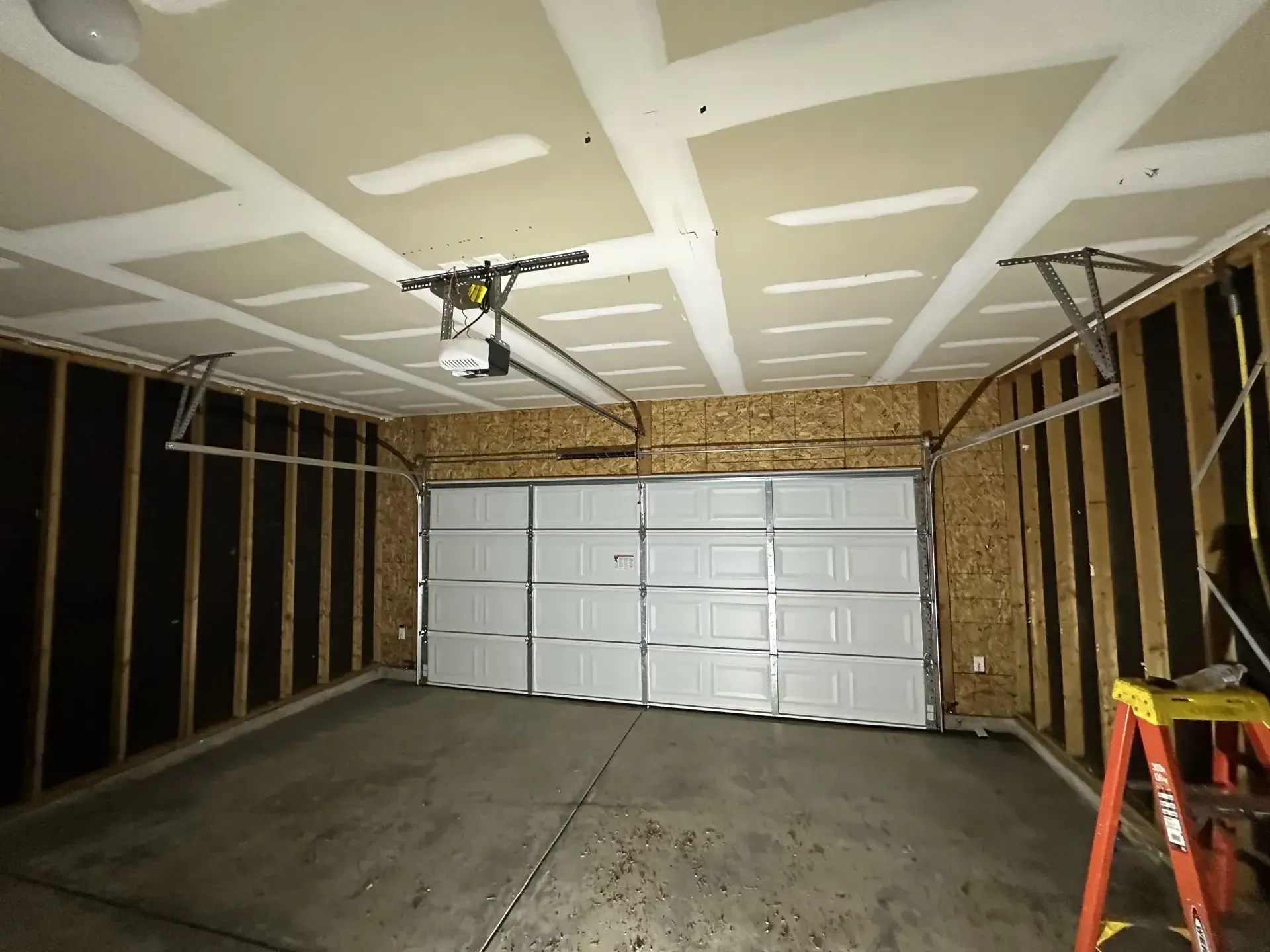 An empty garage with a garage door open and a ladder