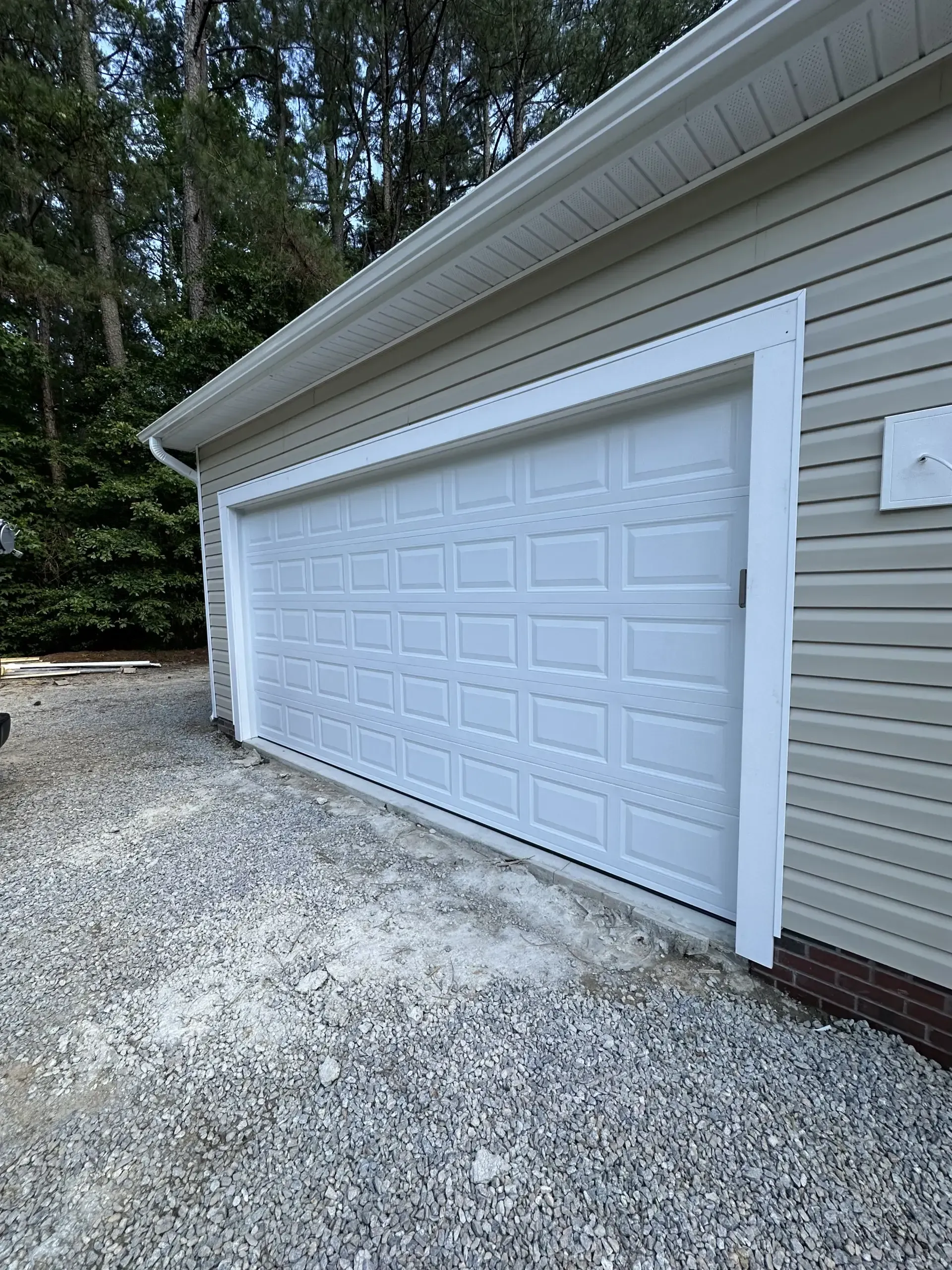 A white garage door is sitting on top of a gravel driveway next to a house.