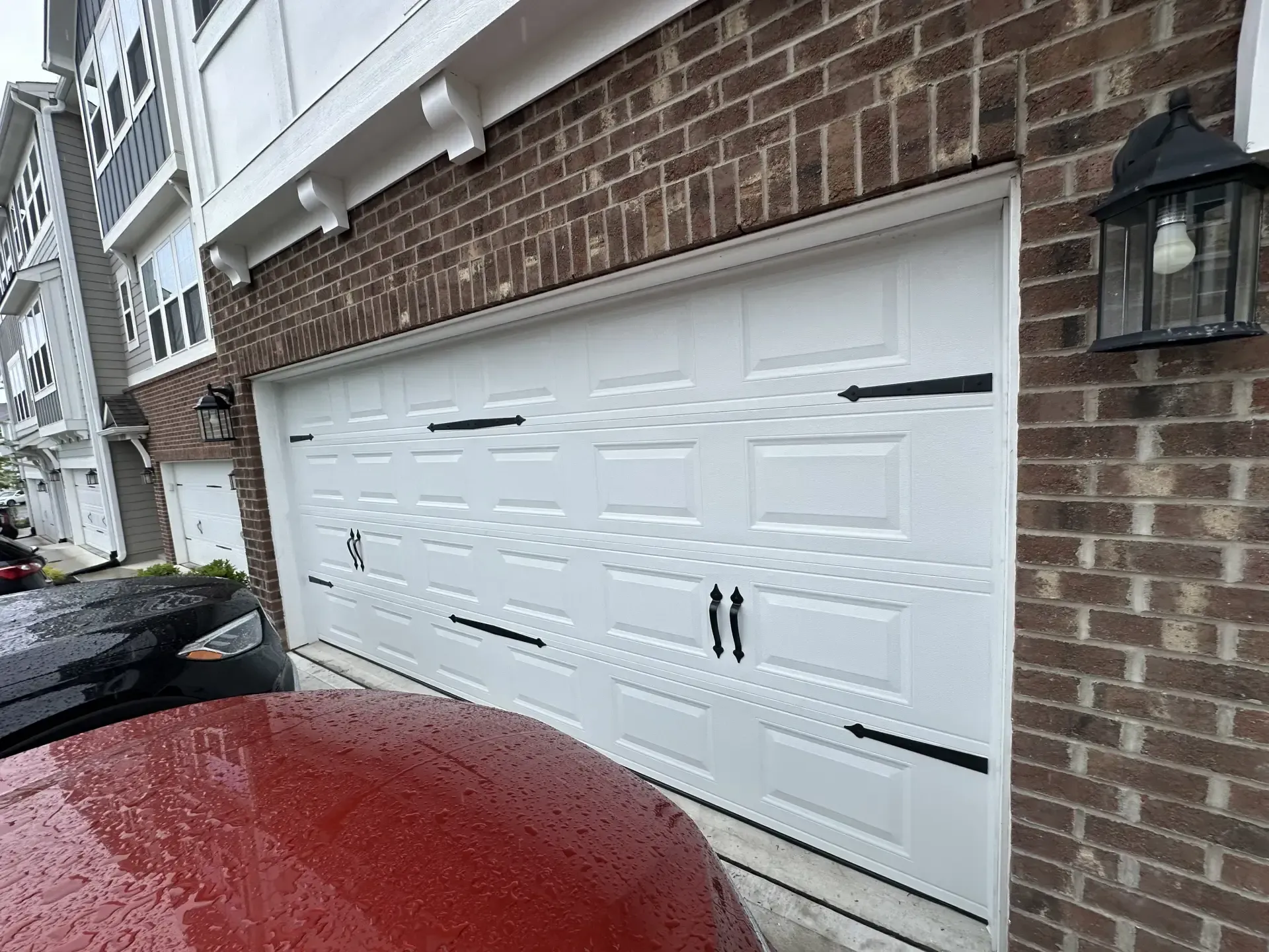A white garage door is sitting on the side of a brick building next to a red car.