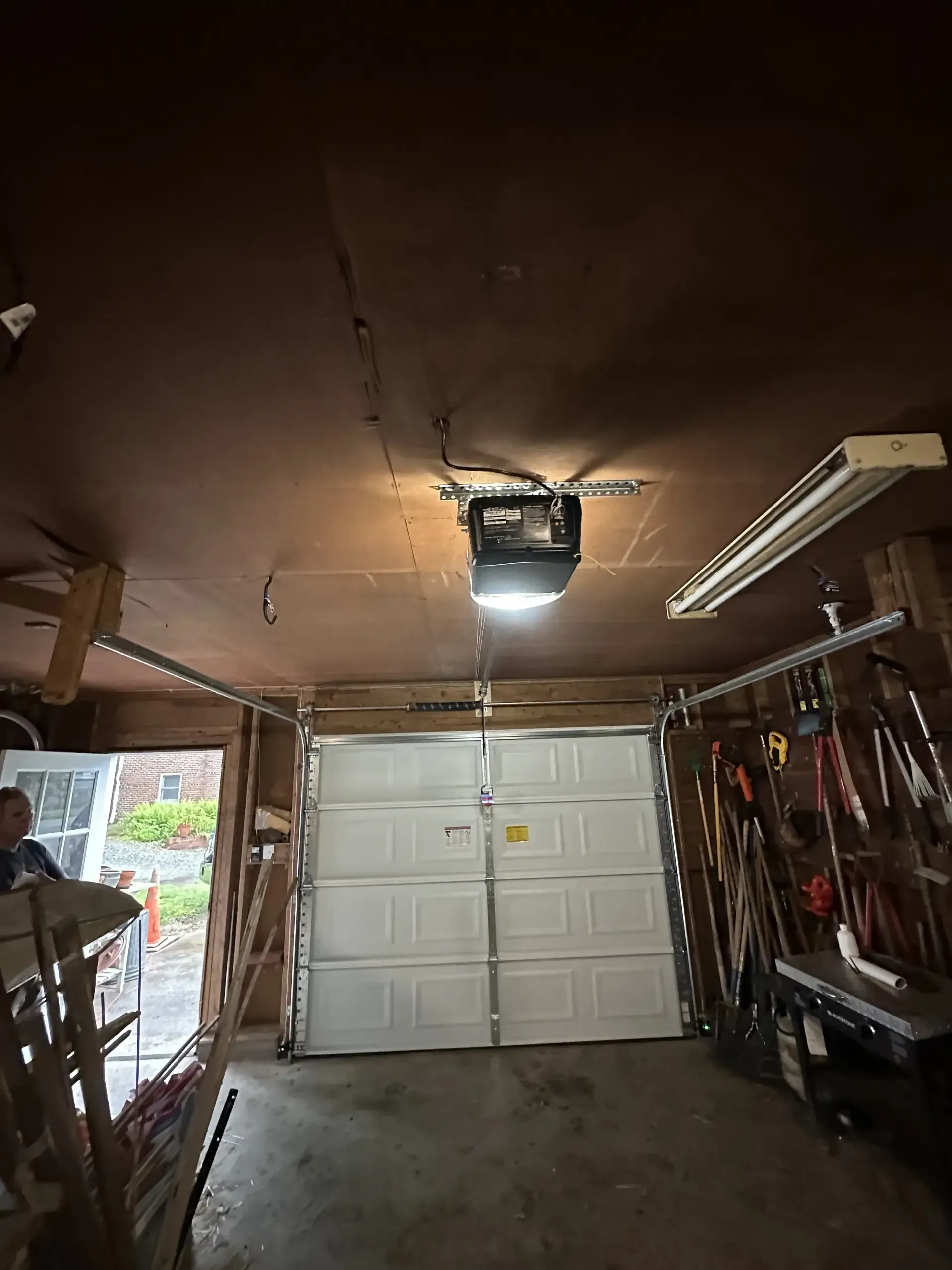 A man is standing in a garage with a garage door open.