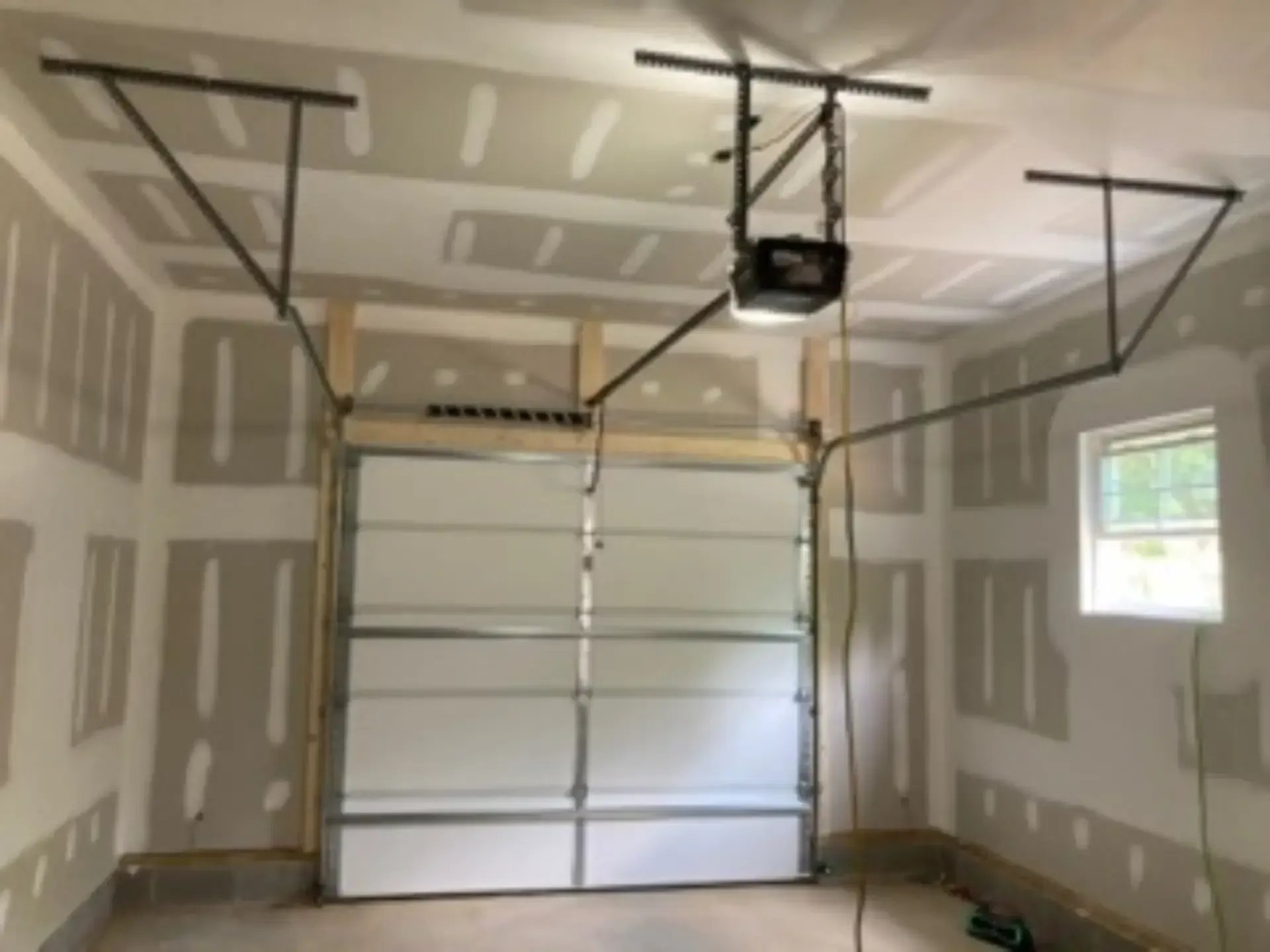 A garage with a garage door open and a garage door opener hanging from the ceiling