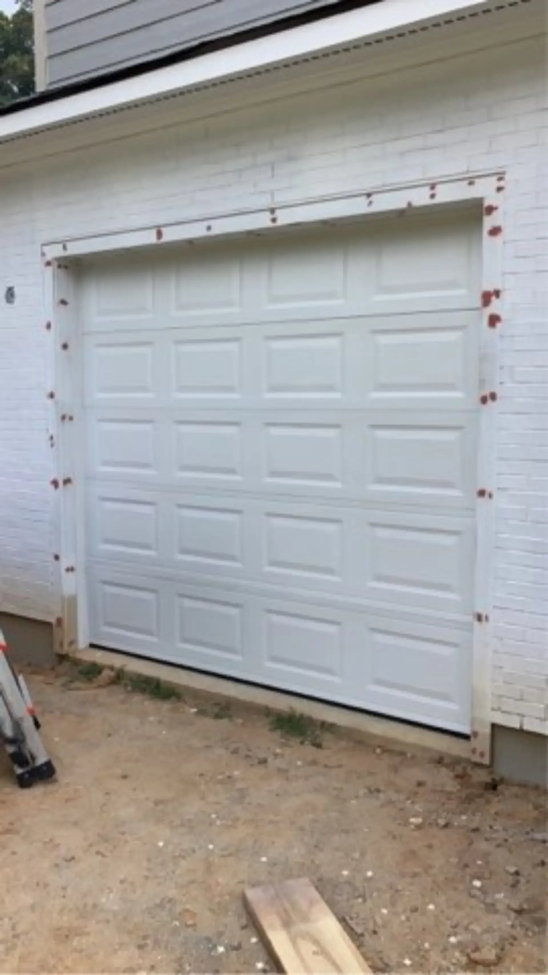 A white garage door is being installed on the side of a house.