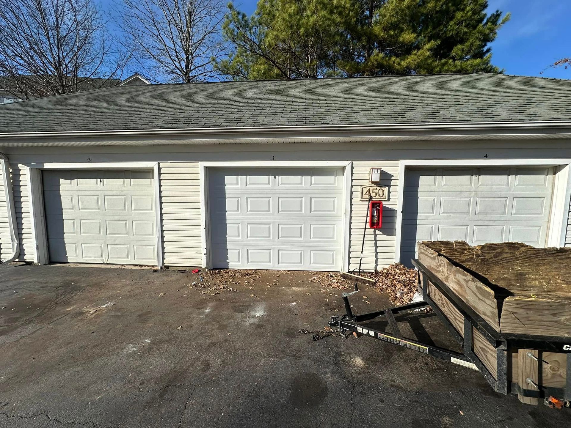 A garage with three white garage doors and a trailer in front of it