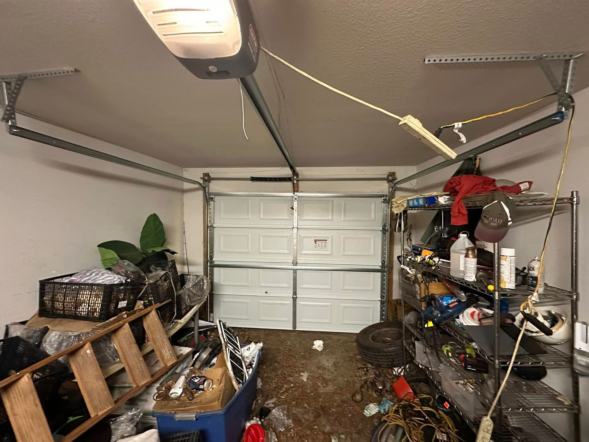 A garage filled with lots of junk and a garage door open.