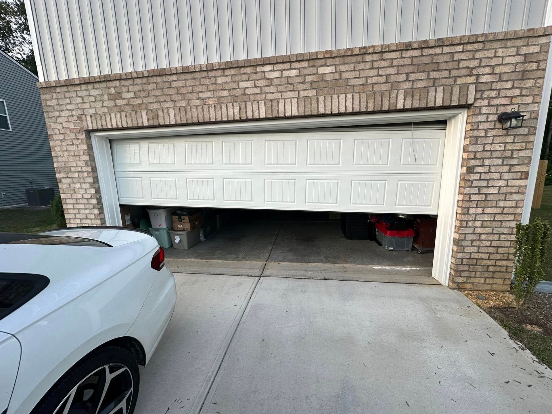 A white car is parked in front of a garage door that is open.