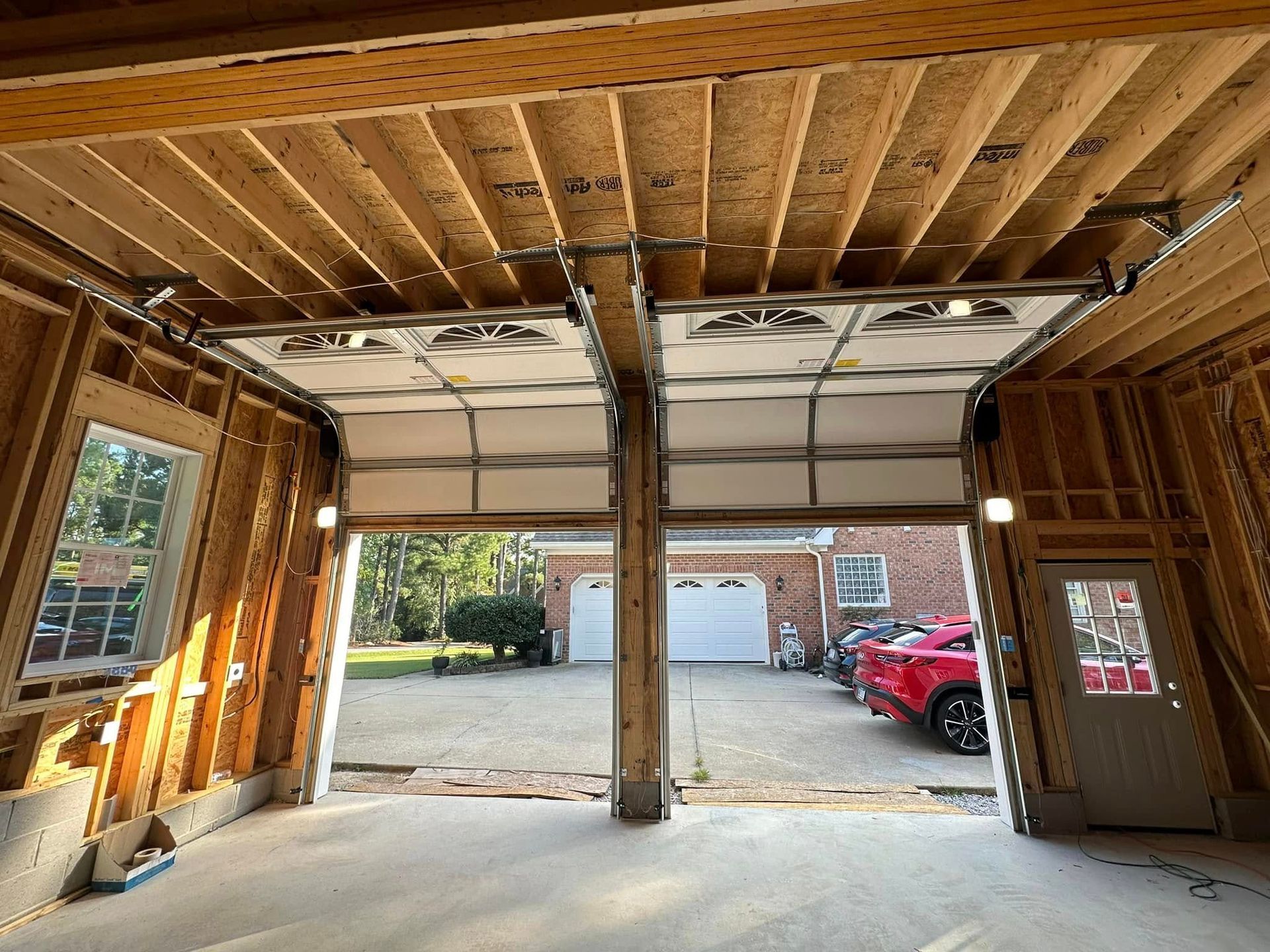 A garage with two garage doors open and a red car parked in the driveway.
