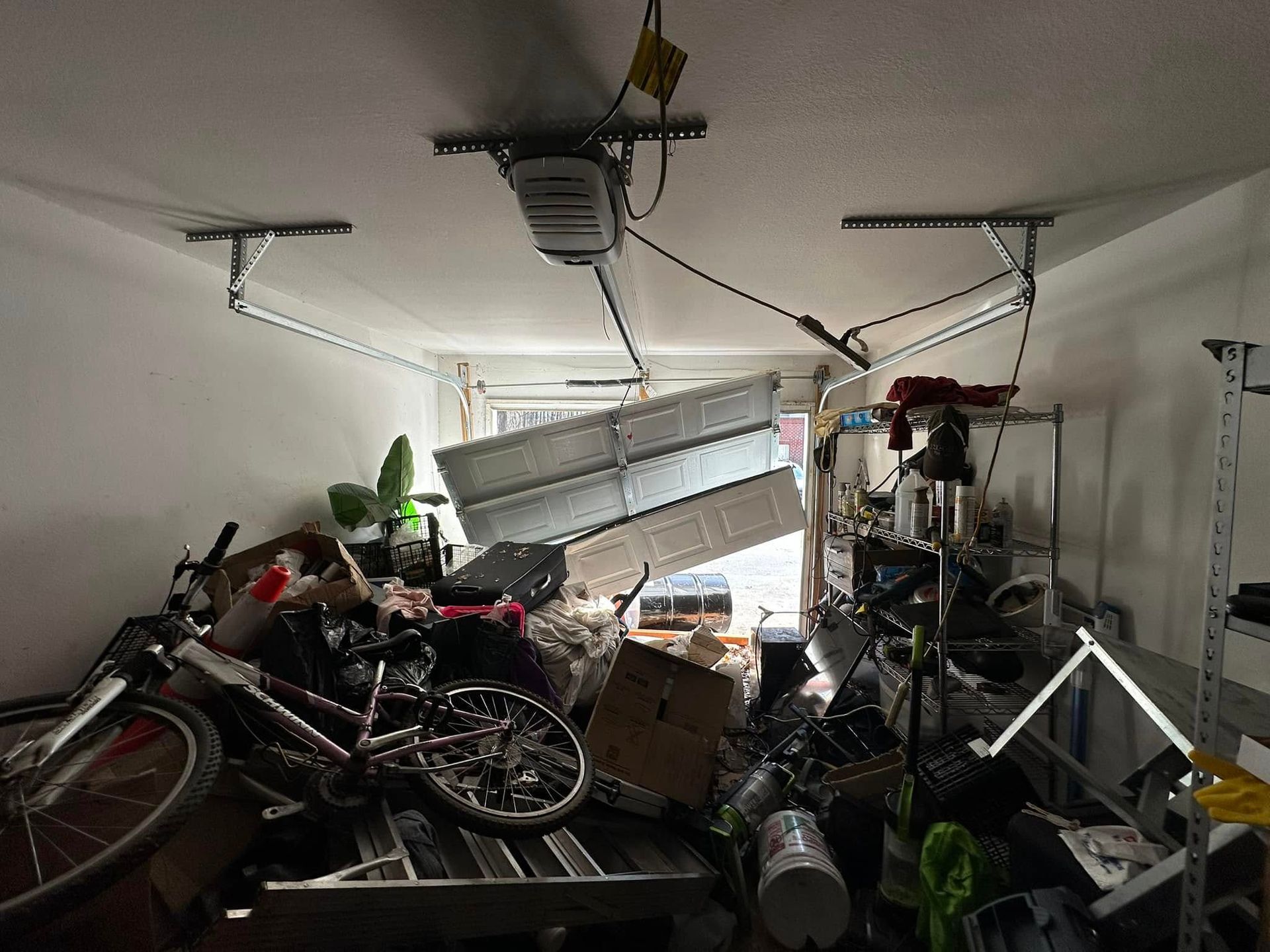 A garage filled with lots of junk and a broken garage door.