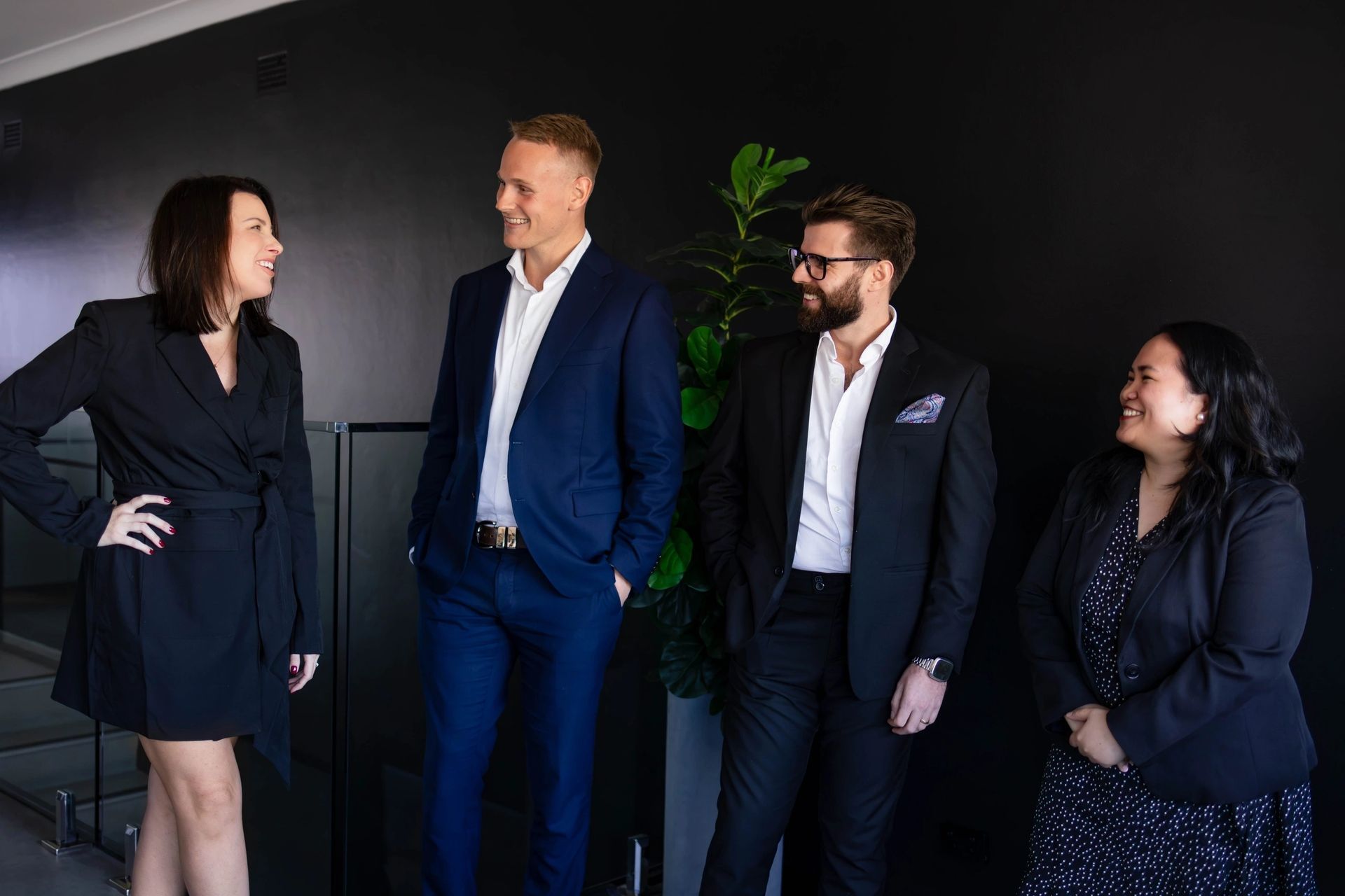 Four people in business attire stand and talk in a modern office.