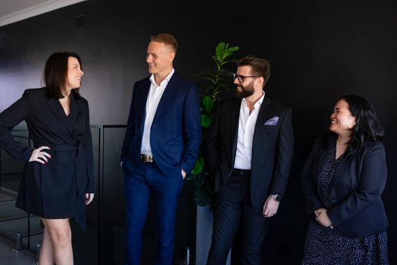Four people in business attire stand and talk in a modern office.