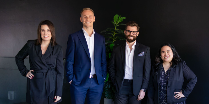 Four people in business attire standing in front of a dark background.