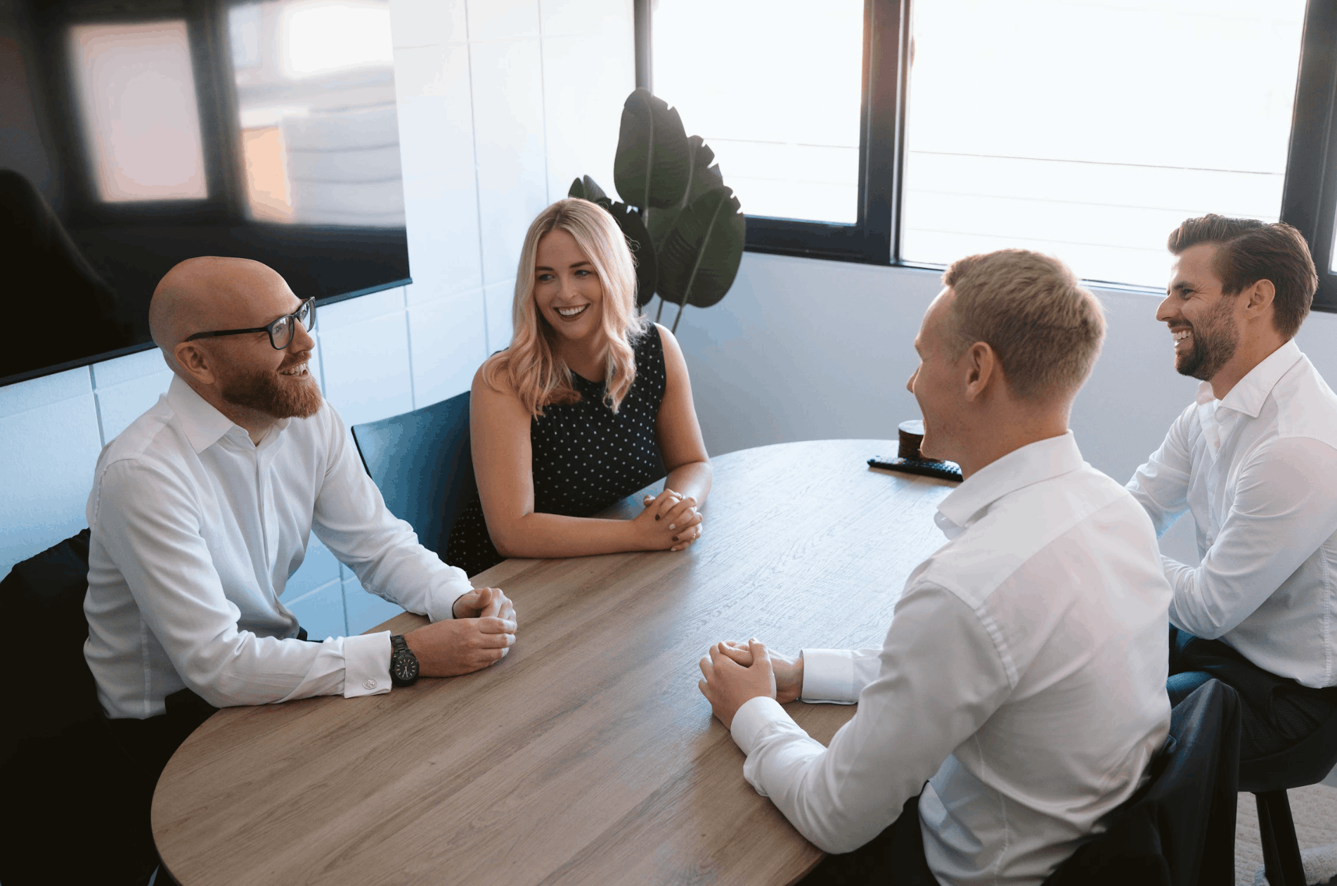 Four people in business attire standing in front of a dark background.
