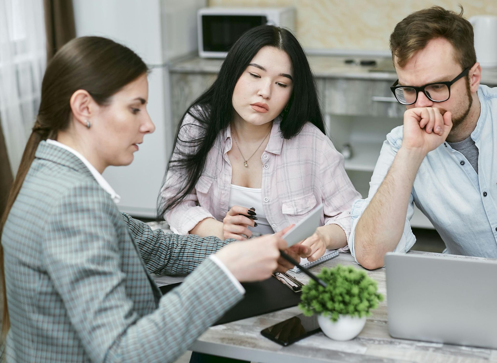 A woman advises a couple at a table, pointing at a document. The couple looks on with concern.
