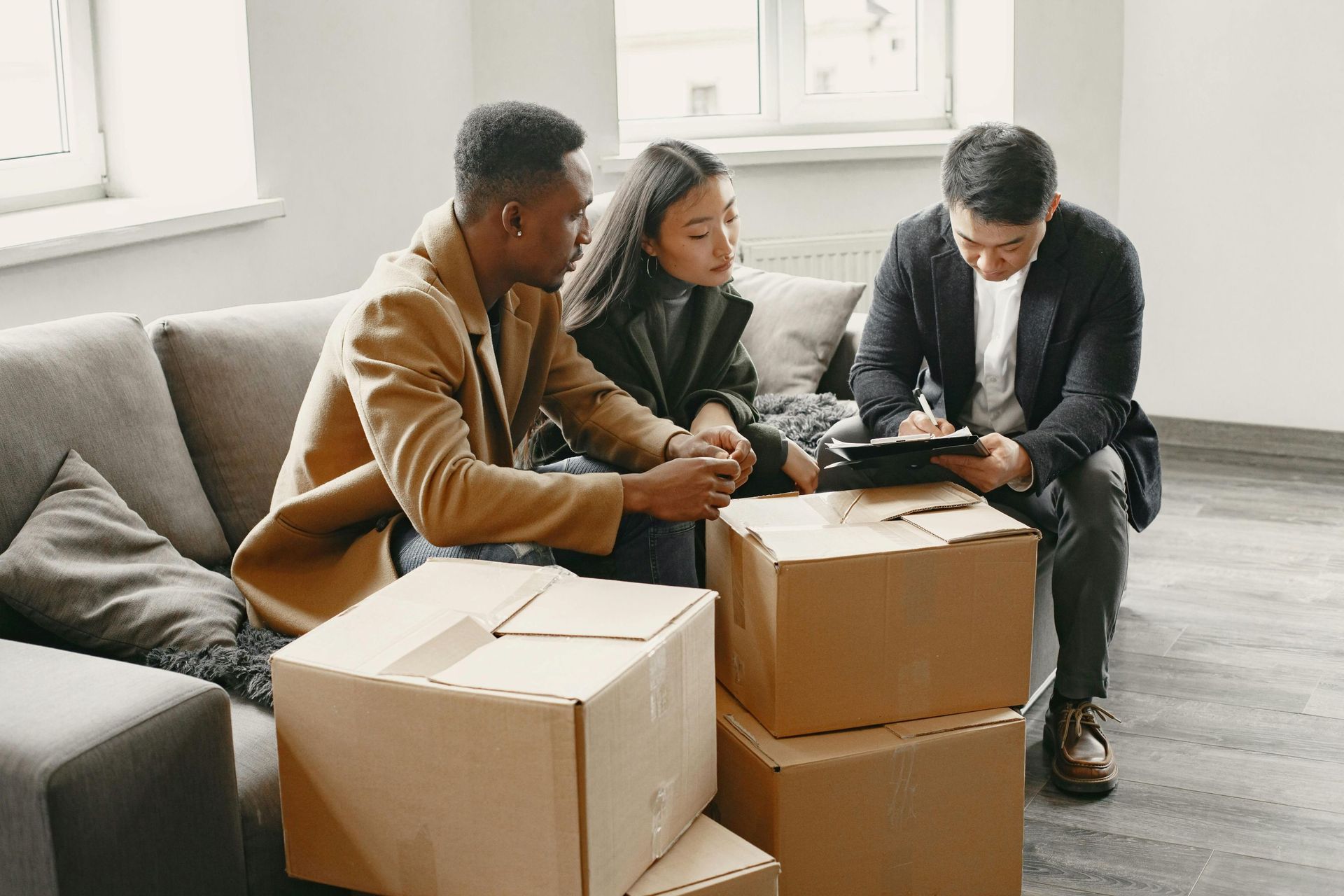 A couple reviews paperwork with a person in a suit, sitting on a couch near moving boxes.