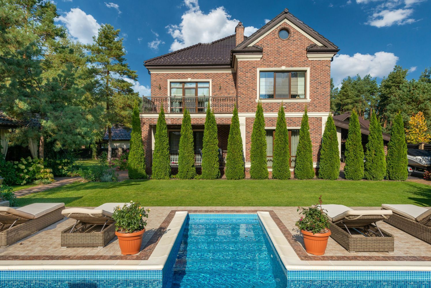 Two-story brick house with a pool in a yard. Green trees and clear blue pool water are in view.