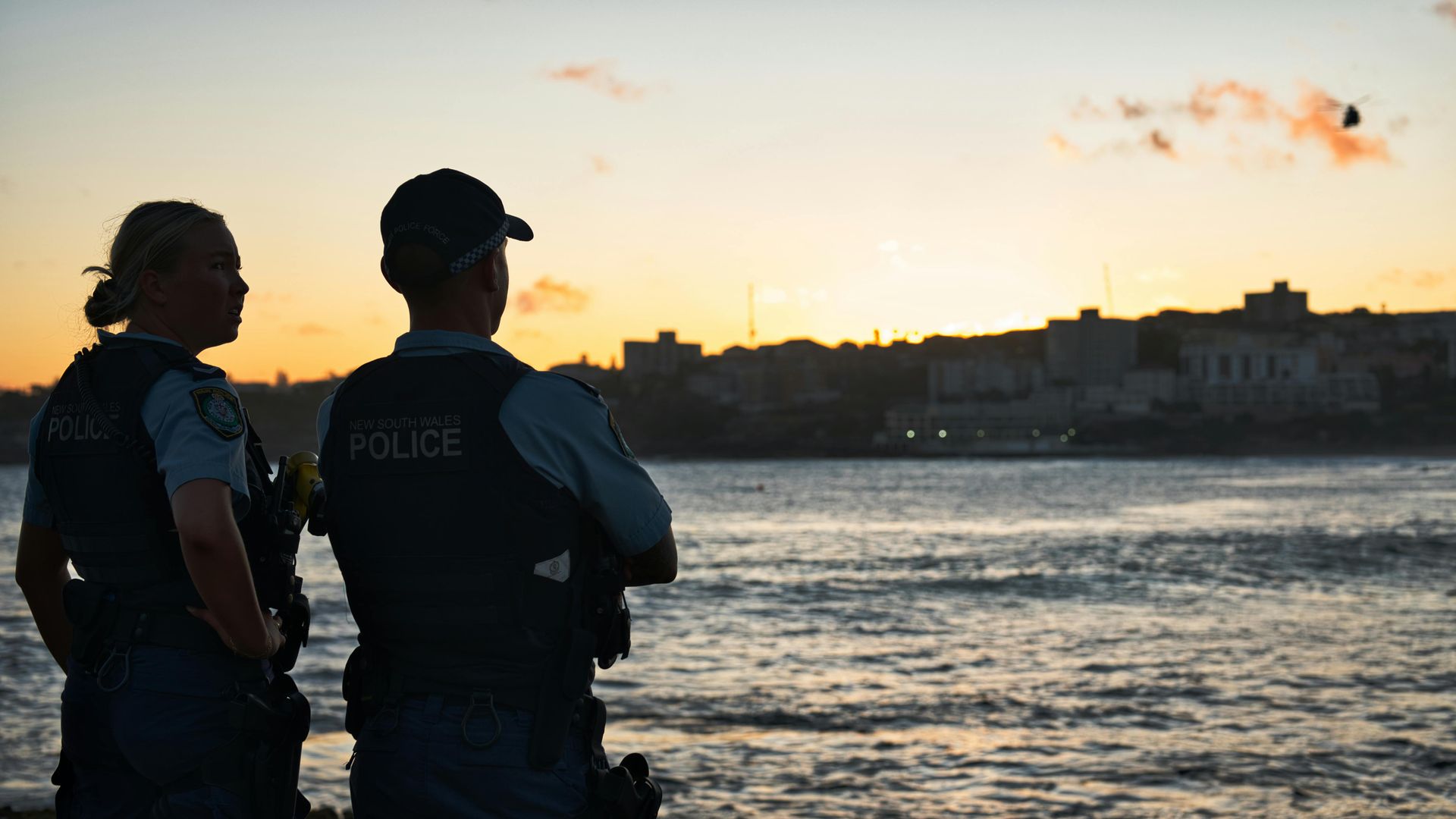 Two police officers watching sunset over water and city skyline.
