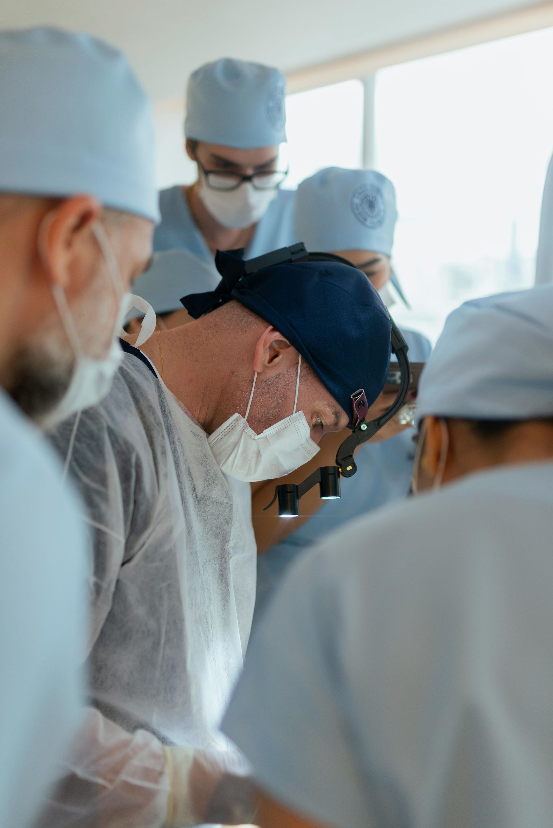 Surgeons in blue scrubs and caps, focused on a procedure in a brightly lit operating room.