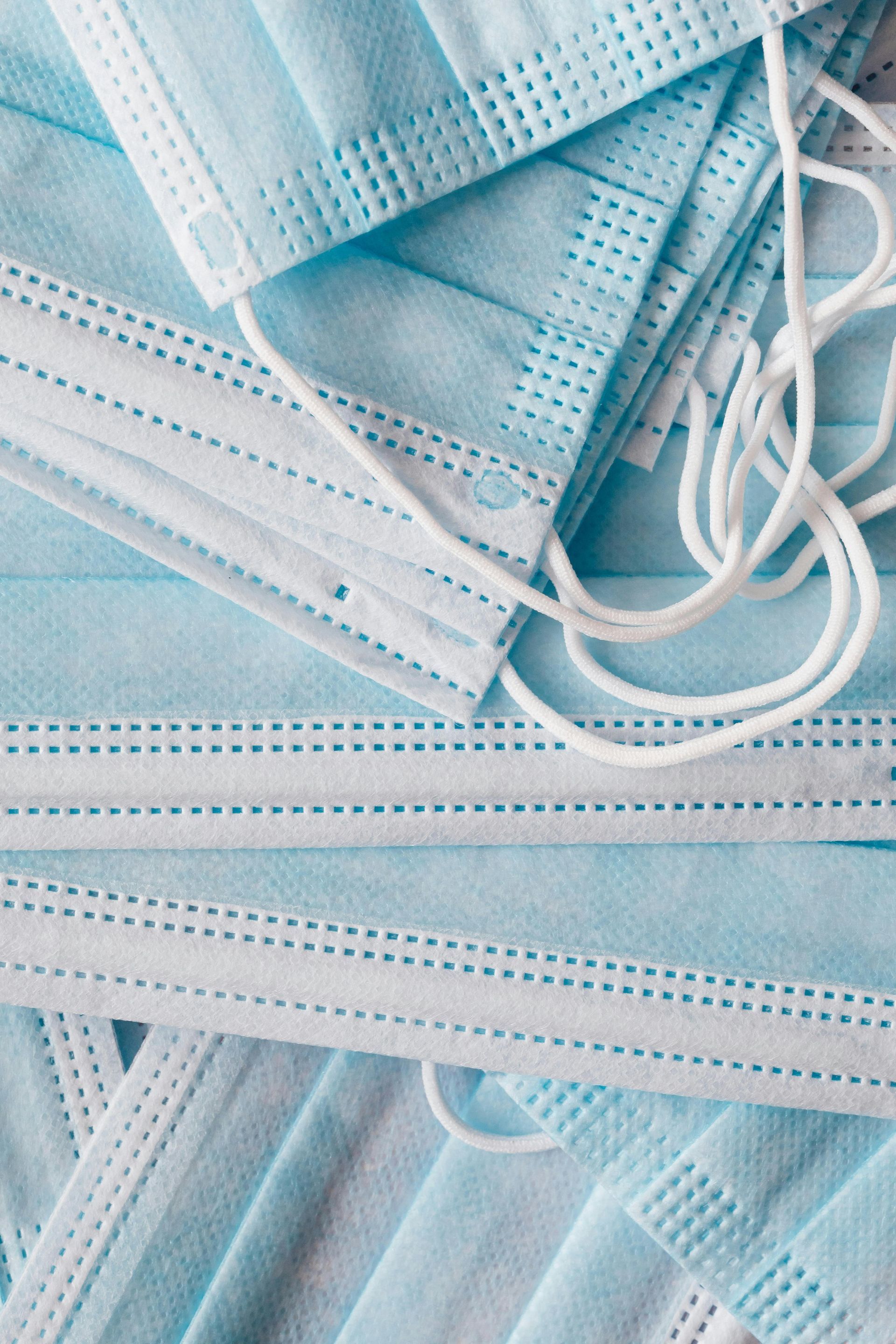 Pile of light blue disposable face masks with white ear loops.