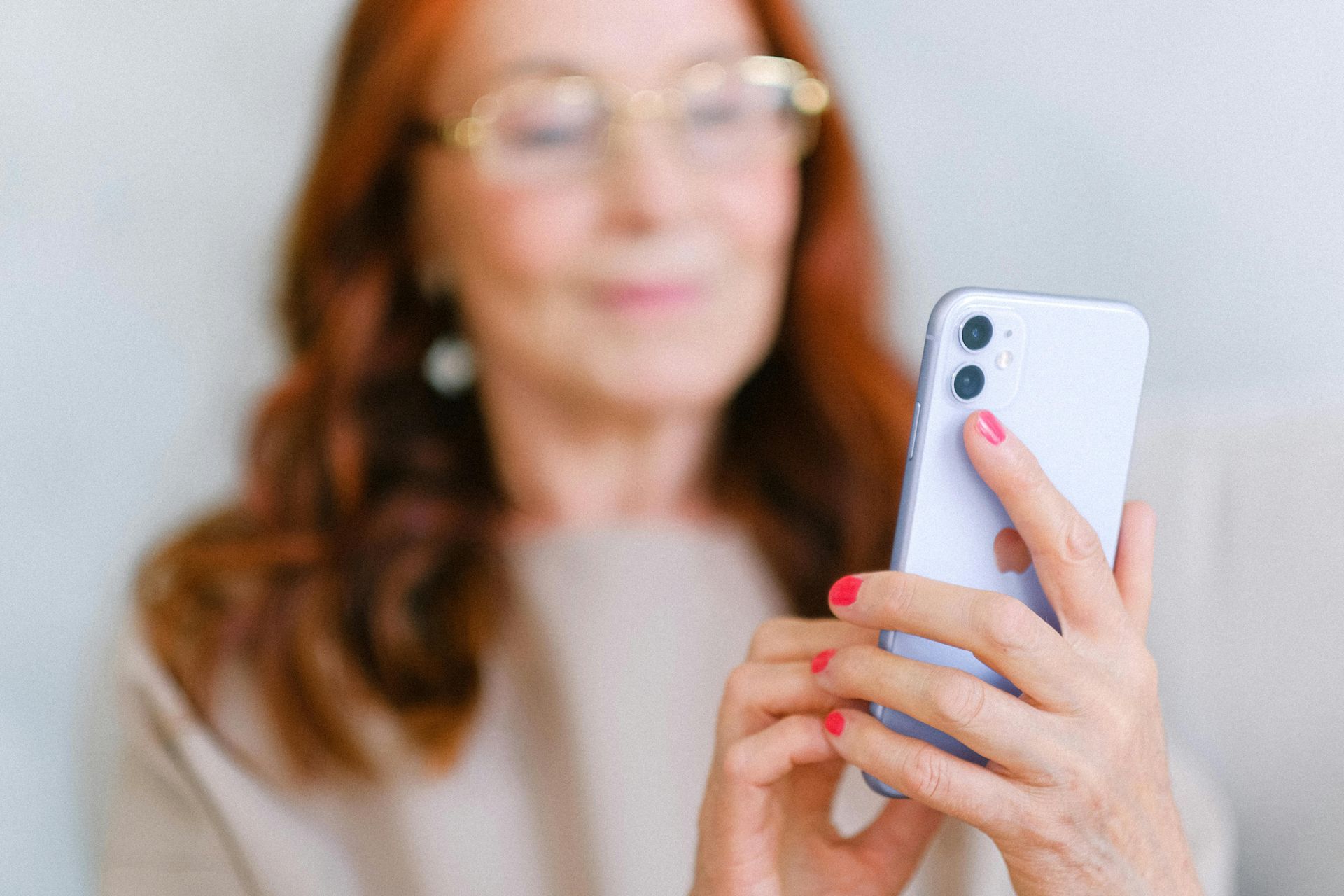 Woman with red hair and glasses using a cell phone; background is blurred.