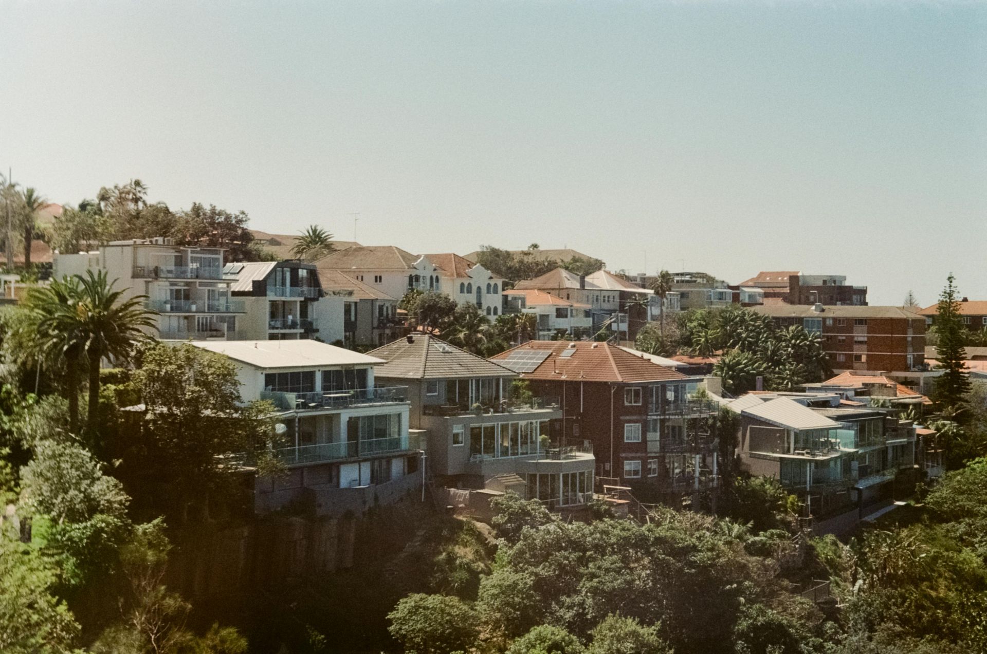 Houses nestled on a hillside with trees, under a clear blue sky.
