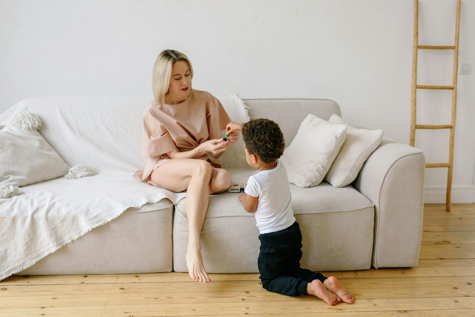 Woman on couch shows something to child kneeling on floor. Indoor setting.