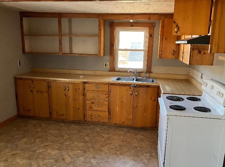 An empty kitchen with wooden cabinets and a white stove.
